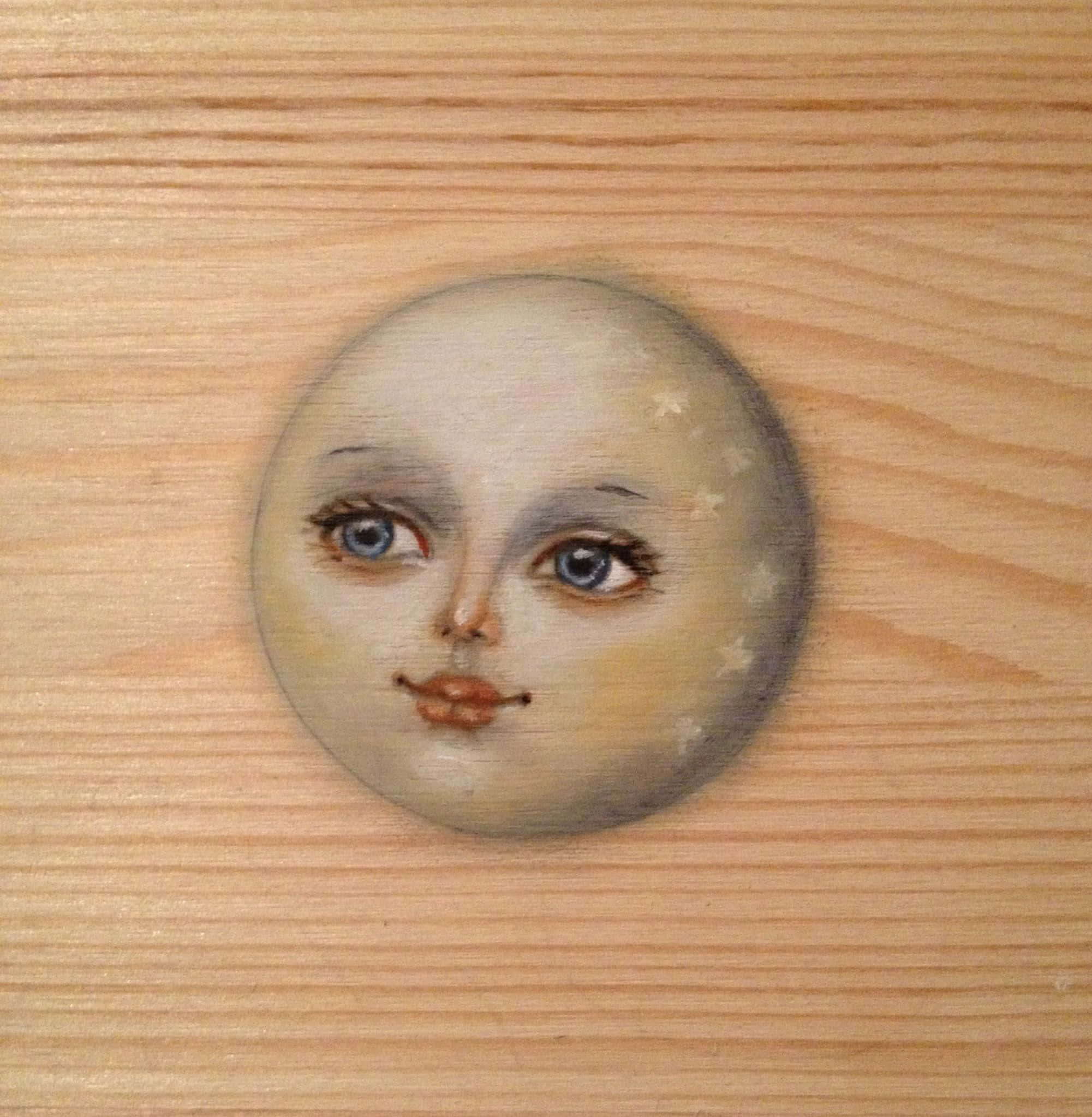 在絢麗夜空下熠熠生輝的月面 壁紙 — 一個繪有藍色眼睛和星星的月亮臉孔放在淺色木質表面上。
