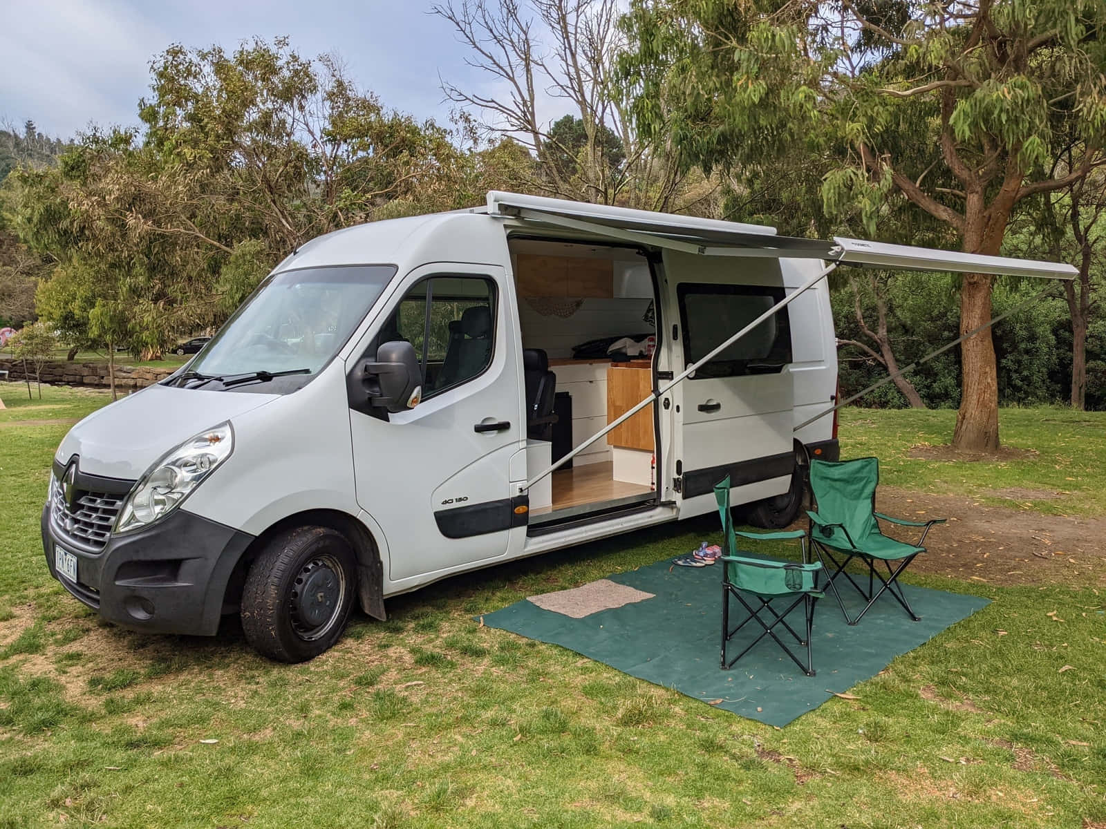 白色露營車停在草地，側門打開，綠色露營椅。