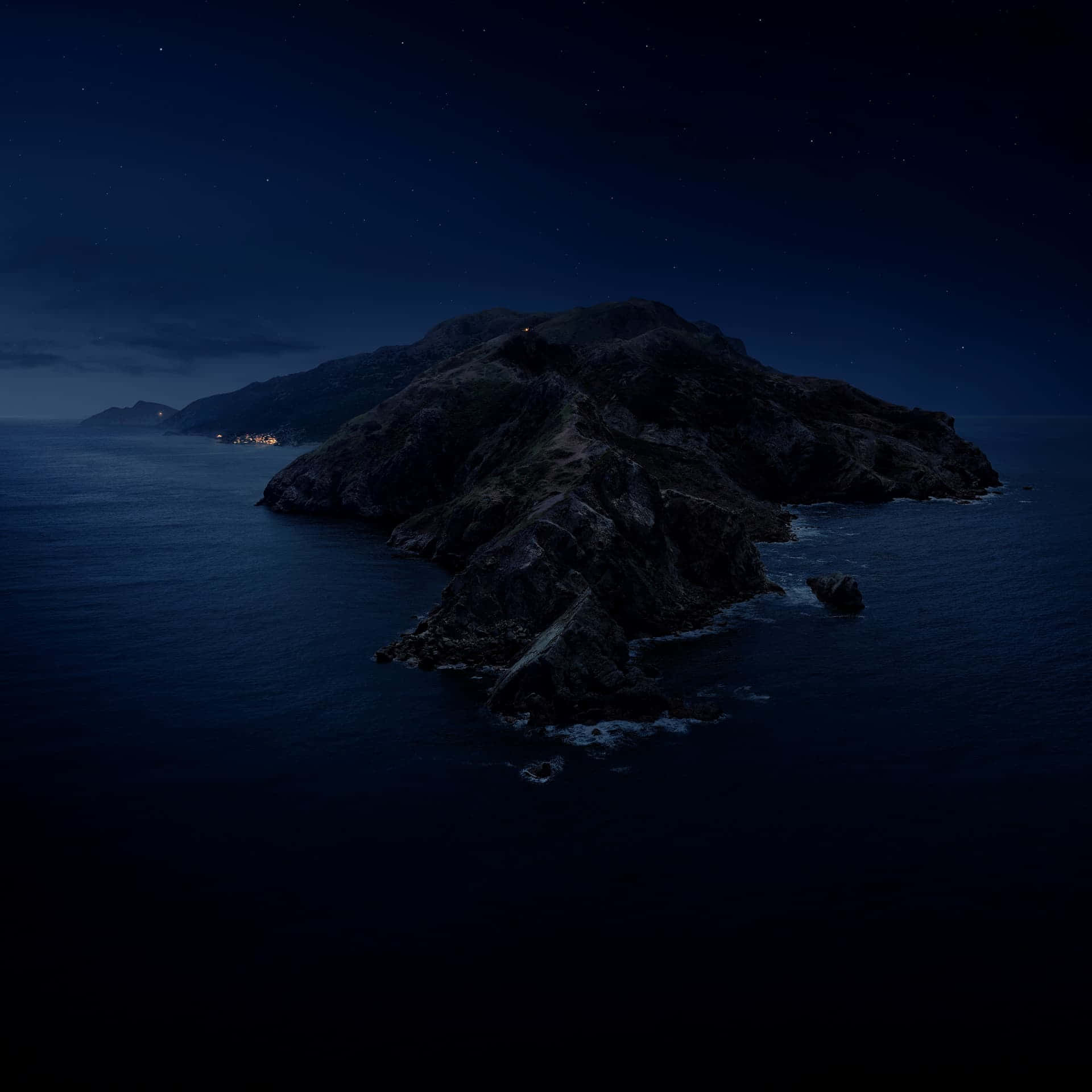 在繁星點點的夜空下，海洋中的一個黑暗岩石島嶼，遠處可見燈光。
