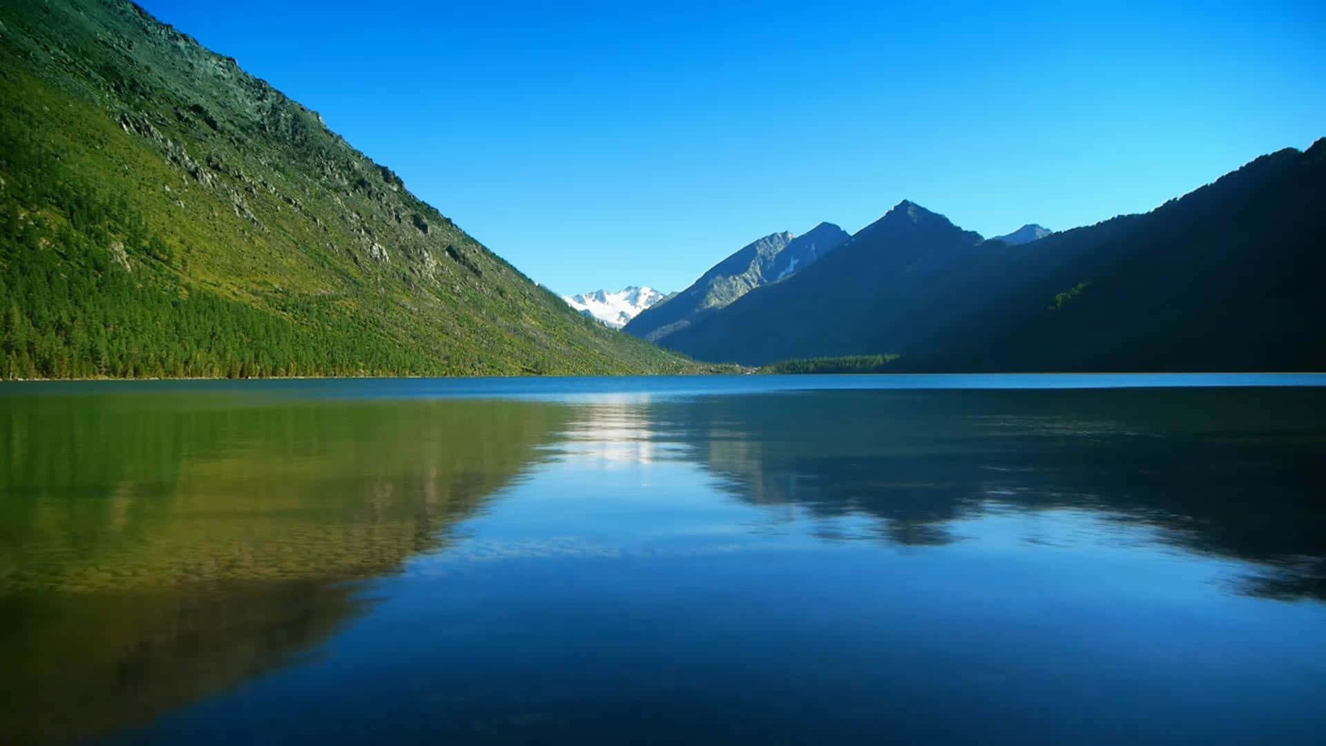 在自然中尋找寧靜 壁紙 — 寧靜的高山湖泊倒映著白雪覆蓋的山峰和翠綠的山坡，在清澈的藍天下。