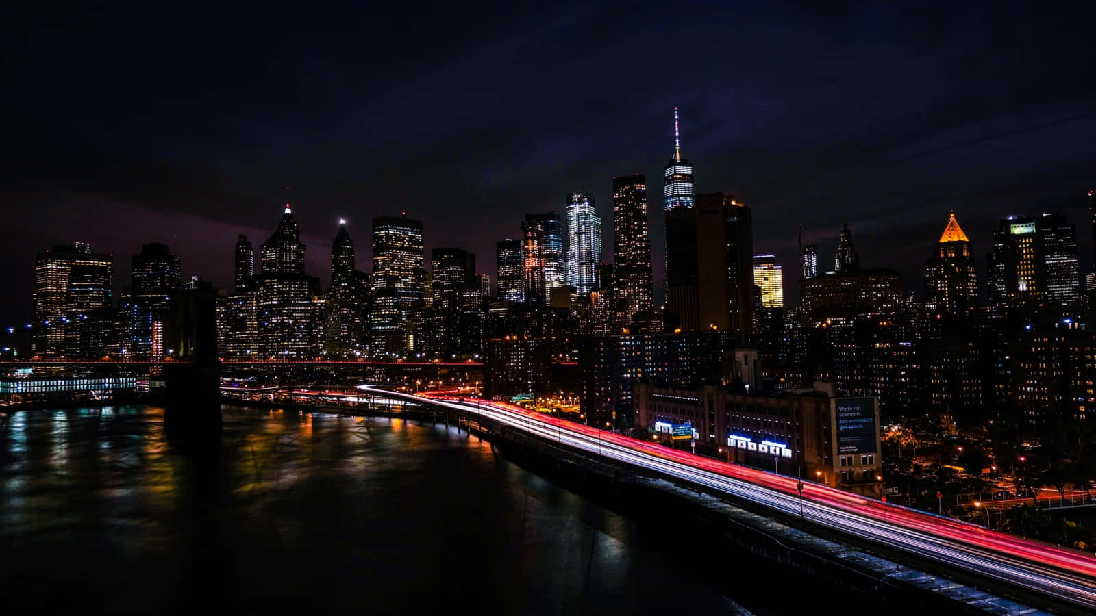 紐約天際線的夜景，建築物燈火通明，橋上的交通燈流動。