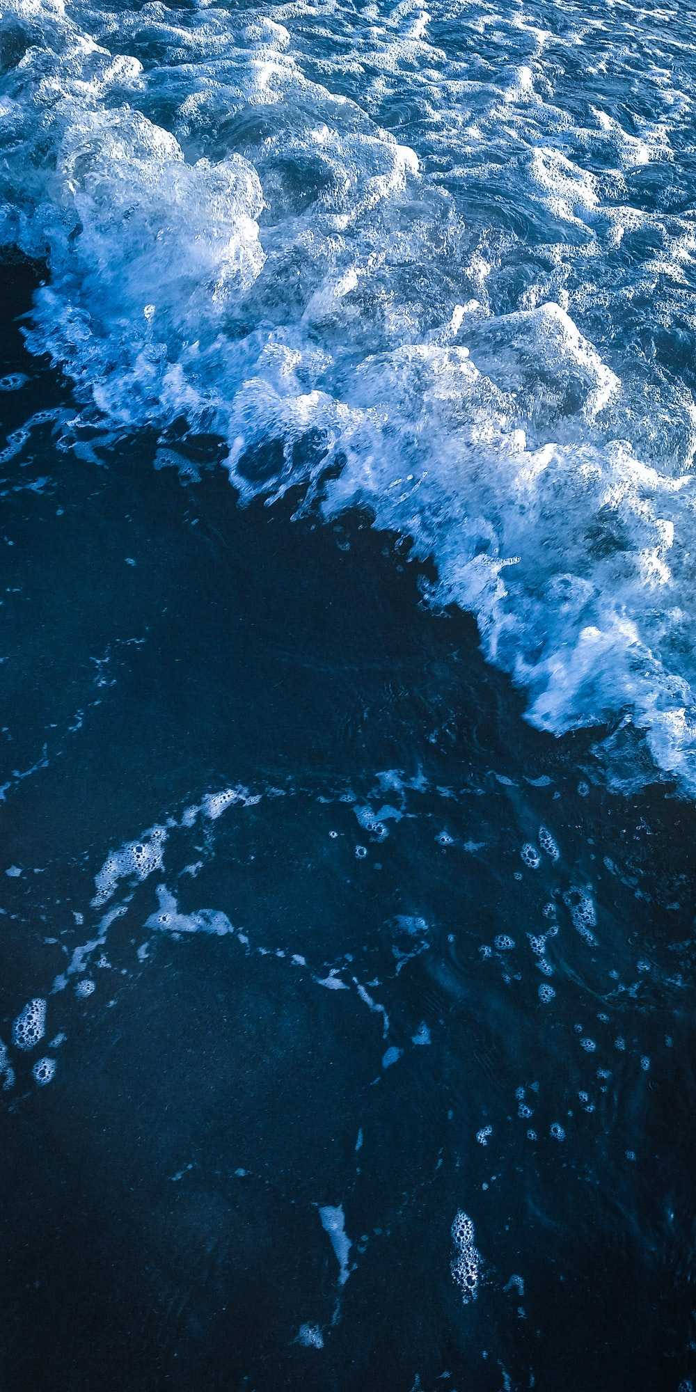 在藍色世界中尋找寧靜 壁紙 — 深藍色海浪拍打黑暗海面、激起白色泡沫的動態特寫。