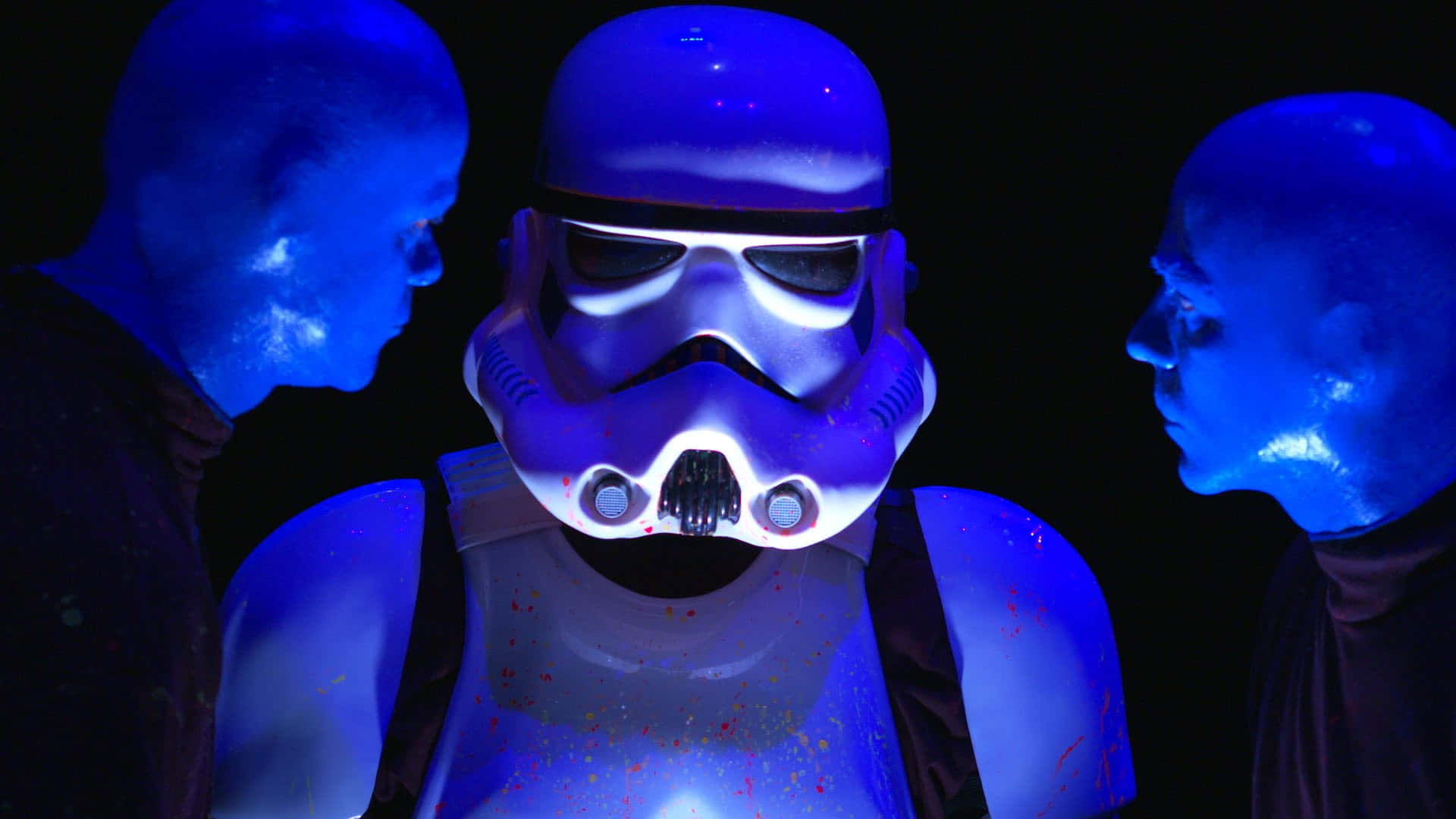 Blue Man Group 桌布 壁紙 — 在藍色照亮的黑暗中，一名風暴兵被兩個光頭、發著藍光的人物夾在中間。