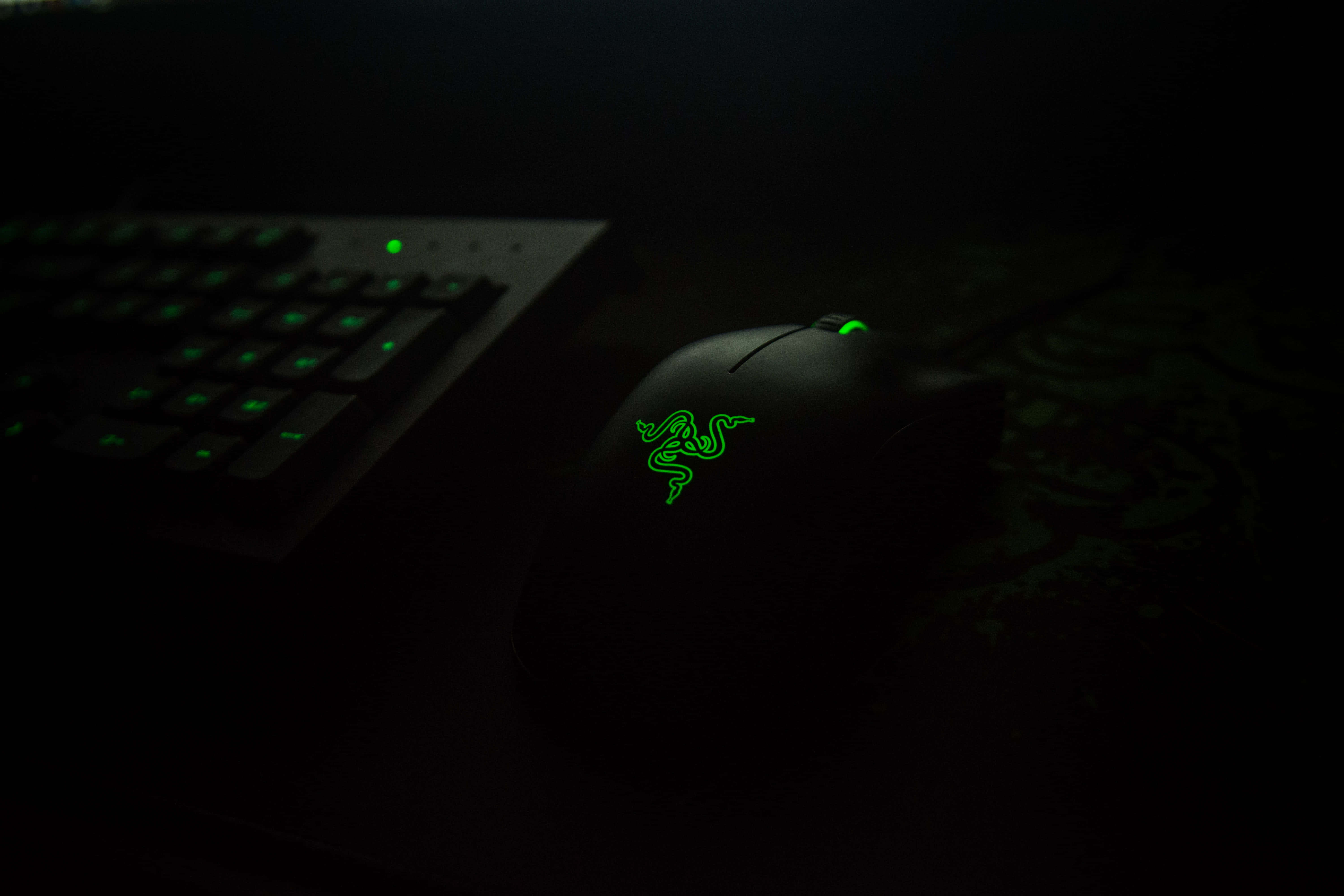 Gaming Mouse 桌布 壁紙 — 在近乎黑暗的環境中，發光的綠色Razer遊戲滑鼠和鍵盤照亮在帶有圖案的表面上。