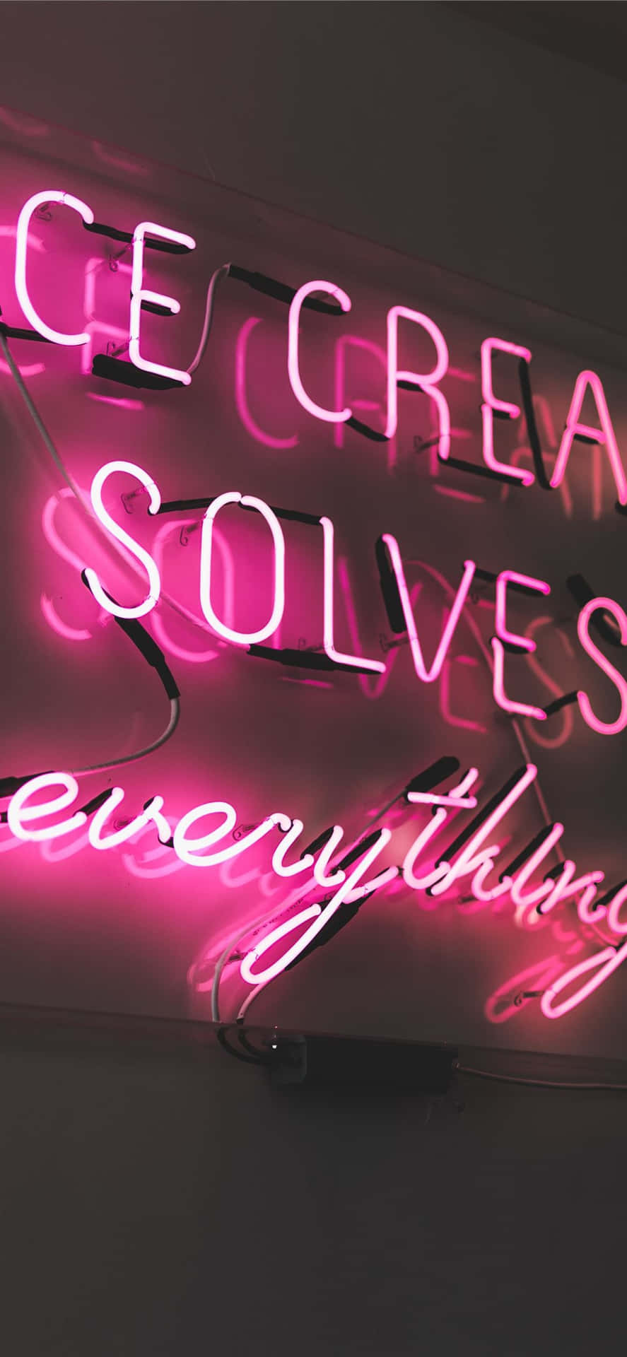 粉紅色霓虹燈牌，上面寫著 ice cream solves everything，掛在深色牆壁上。