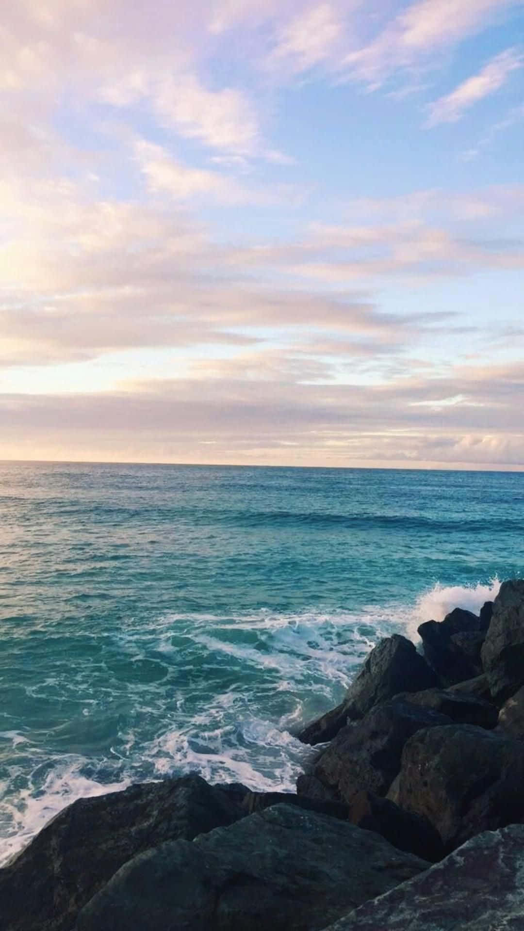 日落時分，海浪拍打深色岩石，天空呈現粉彩色調並伴有雲彩。