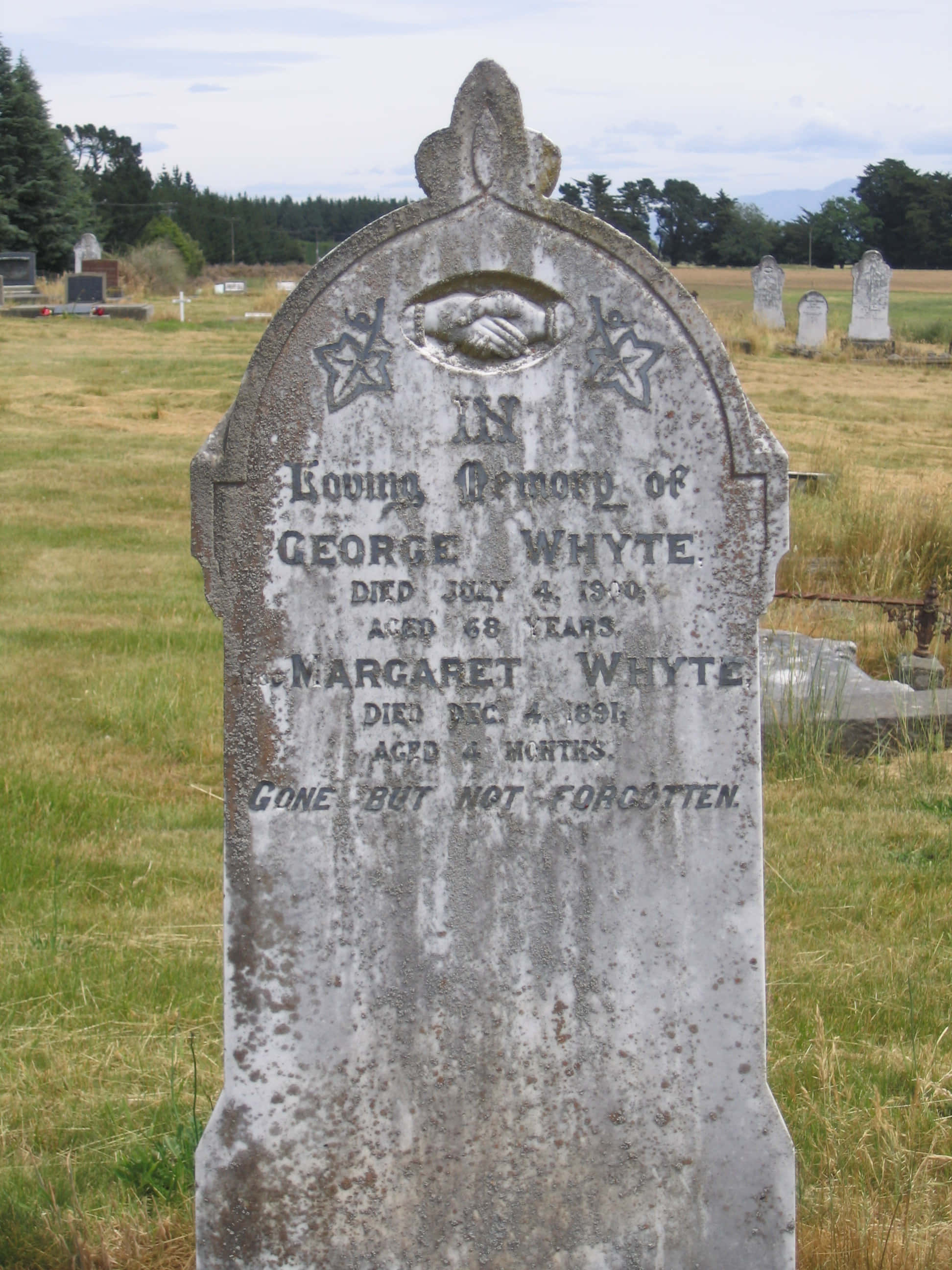 Gravestone 桌布 壁紙 — 在長滿草的墓地中，一塊風化的灰色墓碑以雕刻的星星和握手圖案紀念喬治和瑪格麗特·懷特。