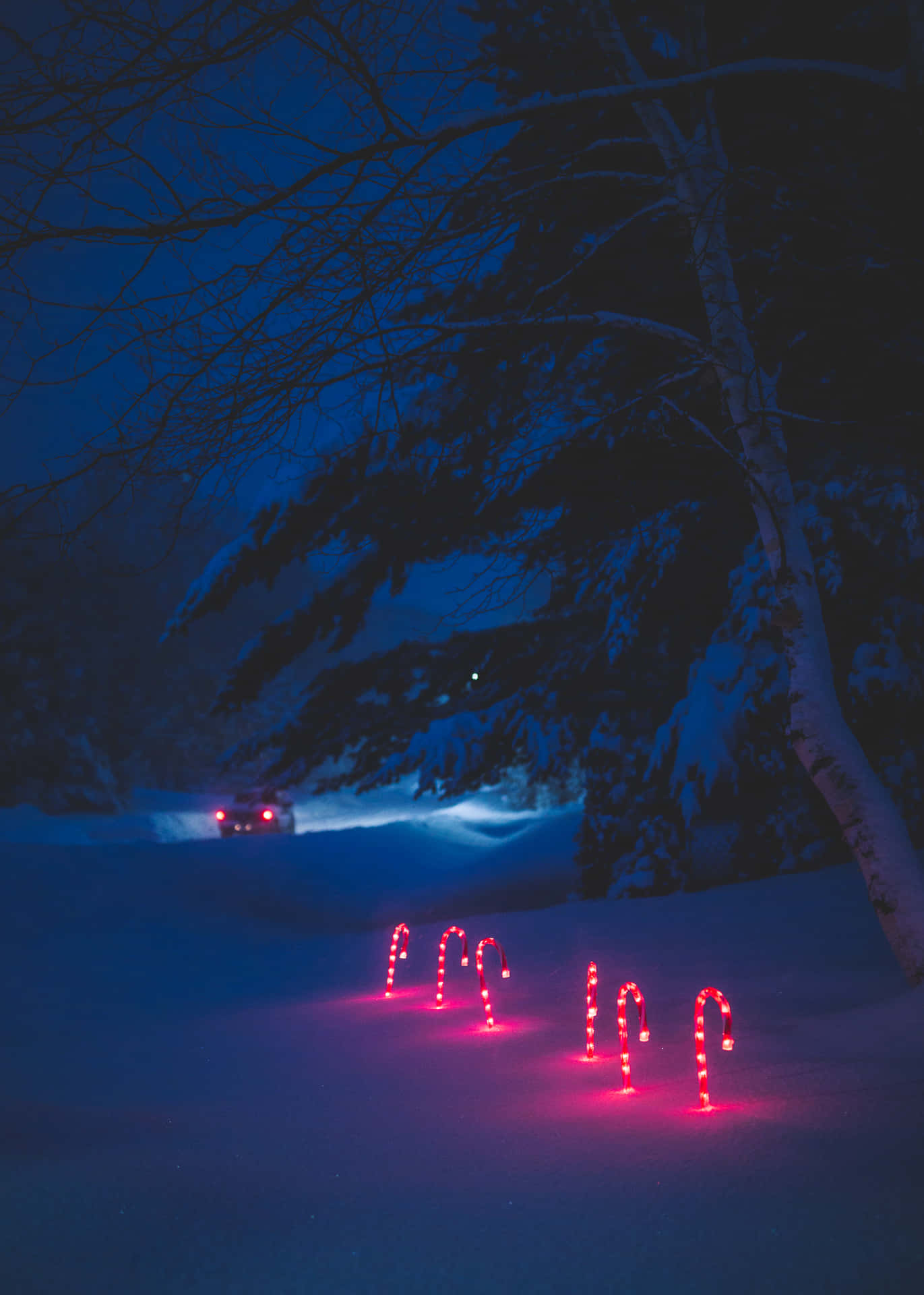 夜間雪中的紅色拐杖糖燈，遠處有一輛汽車。