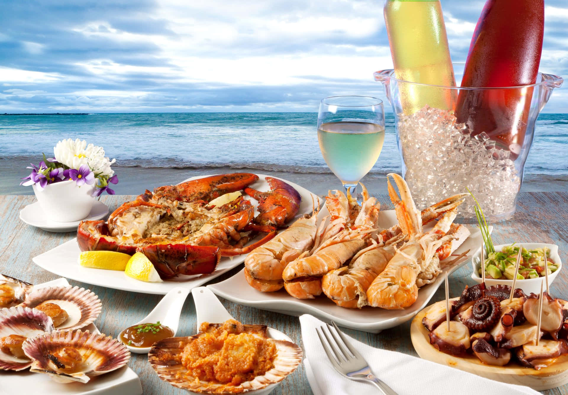 Seafood 桌布 壁紙 — 在陰天之下，一張木桌上擺滿了龍蝦、大蝦、扇貝和八爪魚等豐盛海鮮盛宴，俯瞰平靜的海洋。