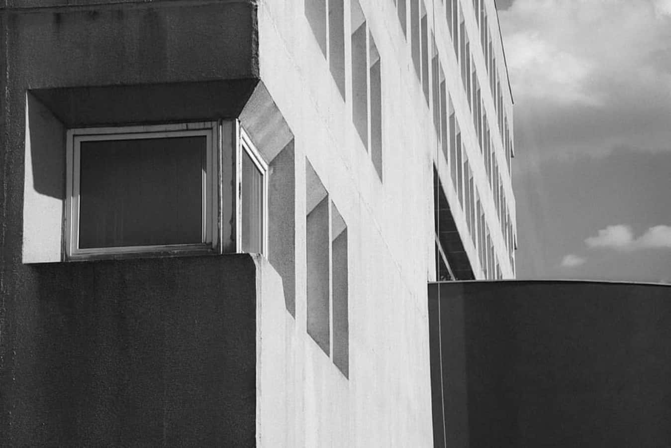 Modernism 桌布 壁紙 — 在陰天天空下，現代主義建築外牆的清晰黑白建築照片，具有幾何窗戶和強烈陰影。
