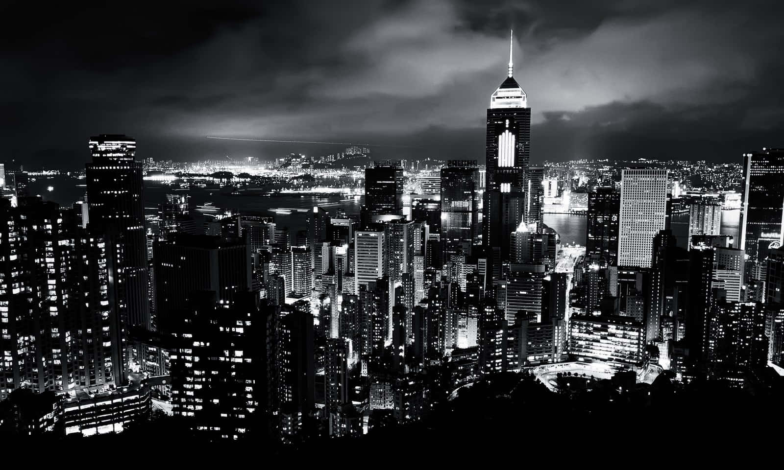 Black And White Cityscape 桌布 壁紙 — 在陰雲密布的天空下，密集的城市天際線、高聳的摩天大樓和發光的窗戶構成的戲劇性黑白夜景。