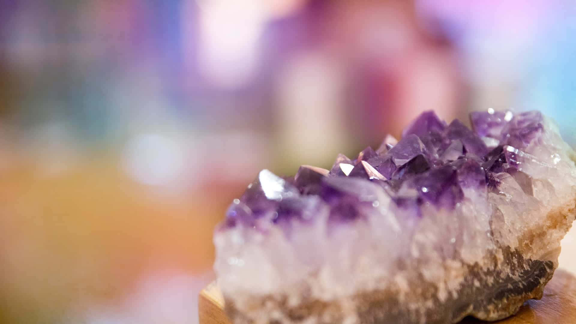 在陽光下閃耀的美麗晶體 壁紙 — 一個閃閃發光的紫水晶晶簇特寫，帶有銳利的紫色刻面，放置在木質底座上，背景柔和模糊。