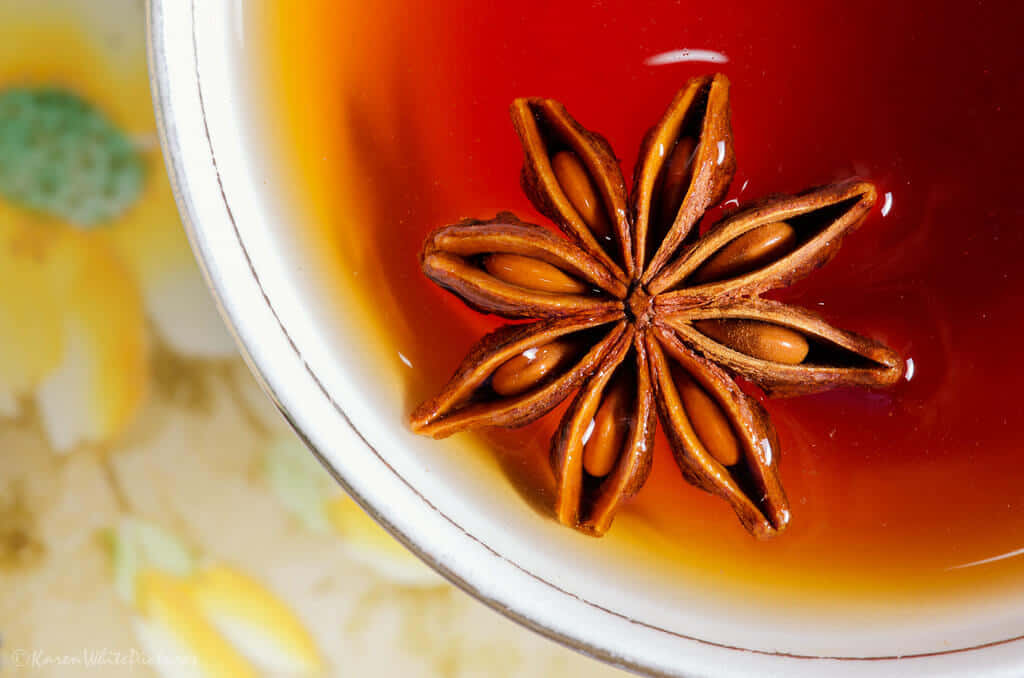 在陽光斑駁的花園中享受一杯溫暖的晨茶 壁紙 — 白陶瓷杯內濃郁琥珀色茶中漂浮的八角特寫。