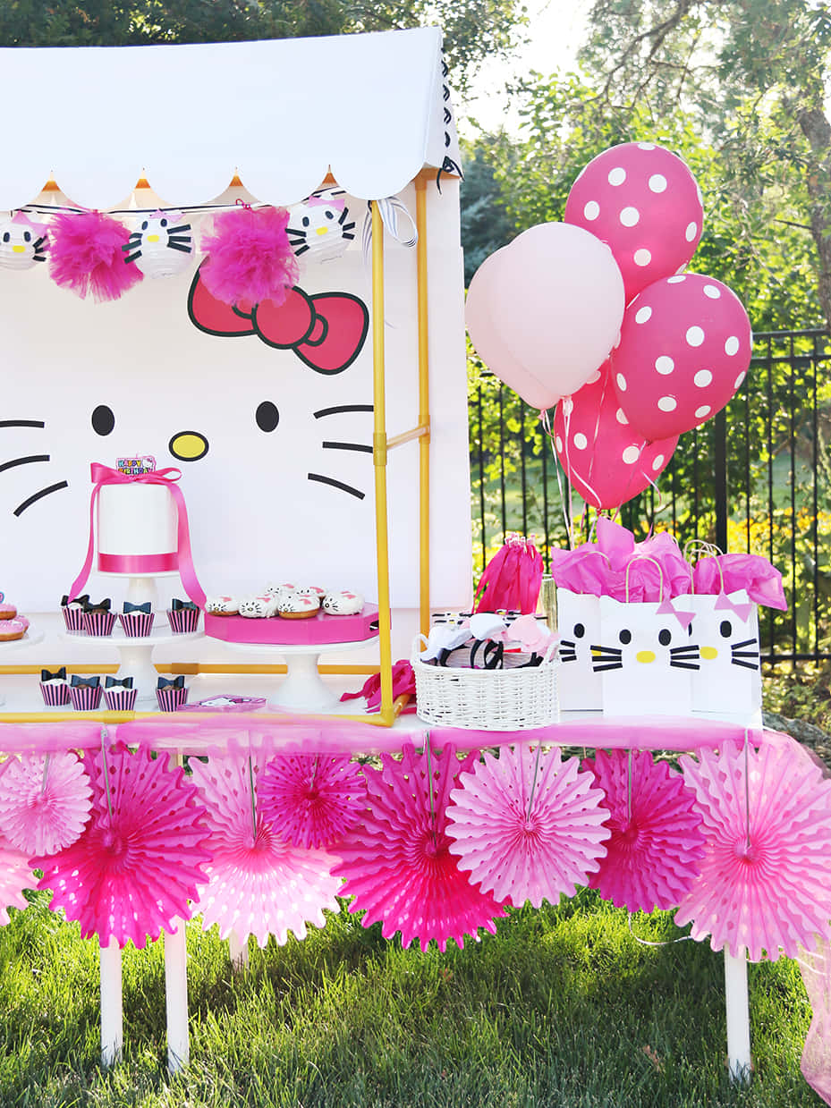 Hello Kitty Party 桌布 壁紙 — 在陽光明媚的戶外天篷下，以粉紅色圓點氣球和紙扇佈置的充滿活力的Hello Kitty生日派對。