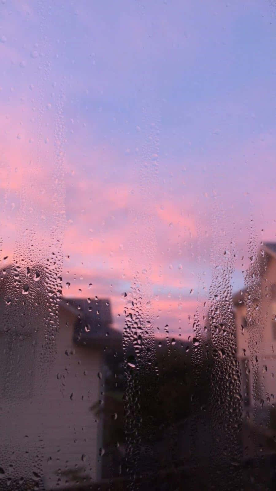 窗上的雨滴，映出屋頂上方粉紅與紫色的夕陽景色。