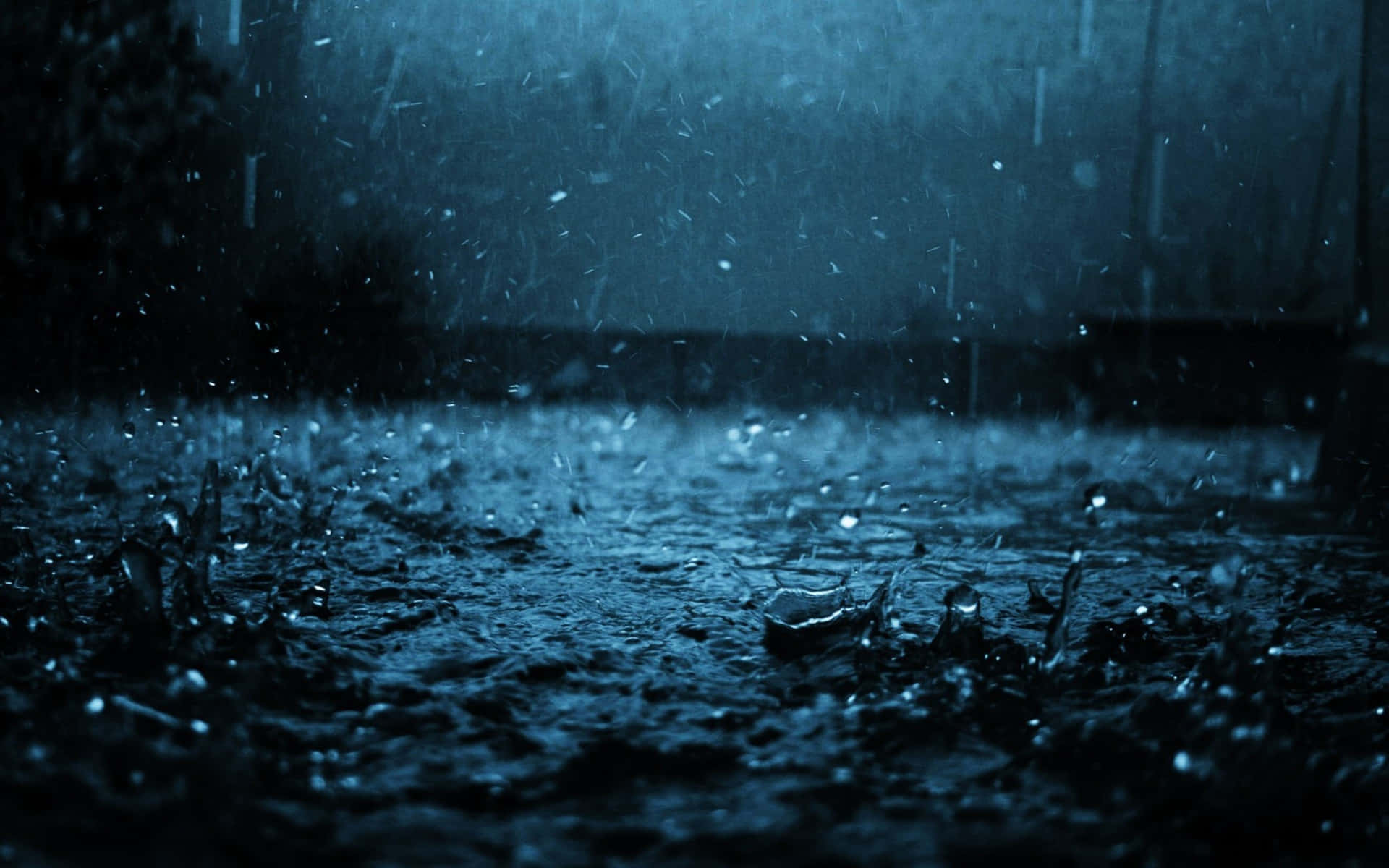 在深藍色夜空下，雨點濺落在潮濕的路面上。