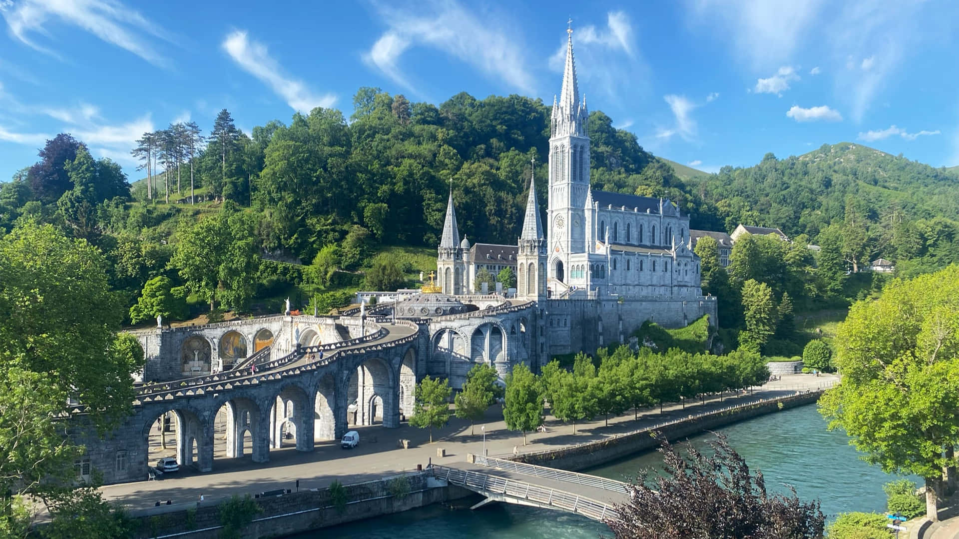 石砌修道院，尖塔俯瞰河流，周圍是綠色的山丘，陽光明媚。