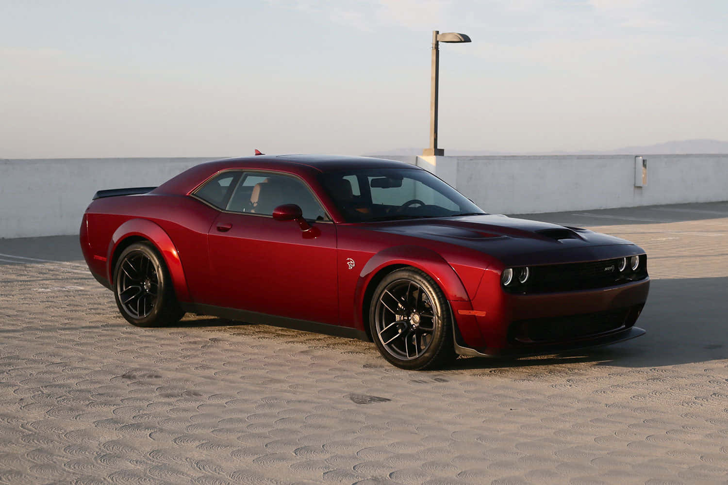 日落時分紋理路面上停泊的紅色Dodge Challenger肌肉車。