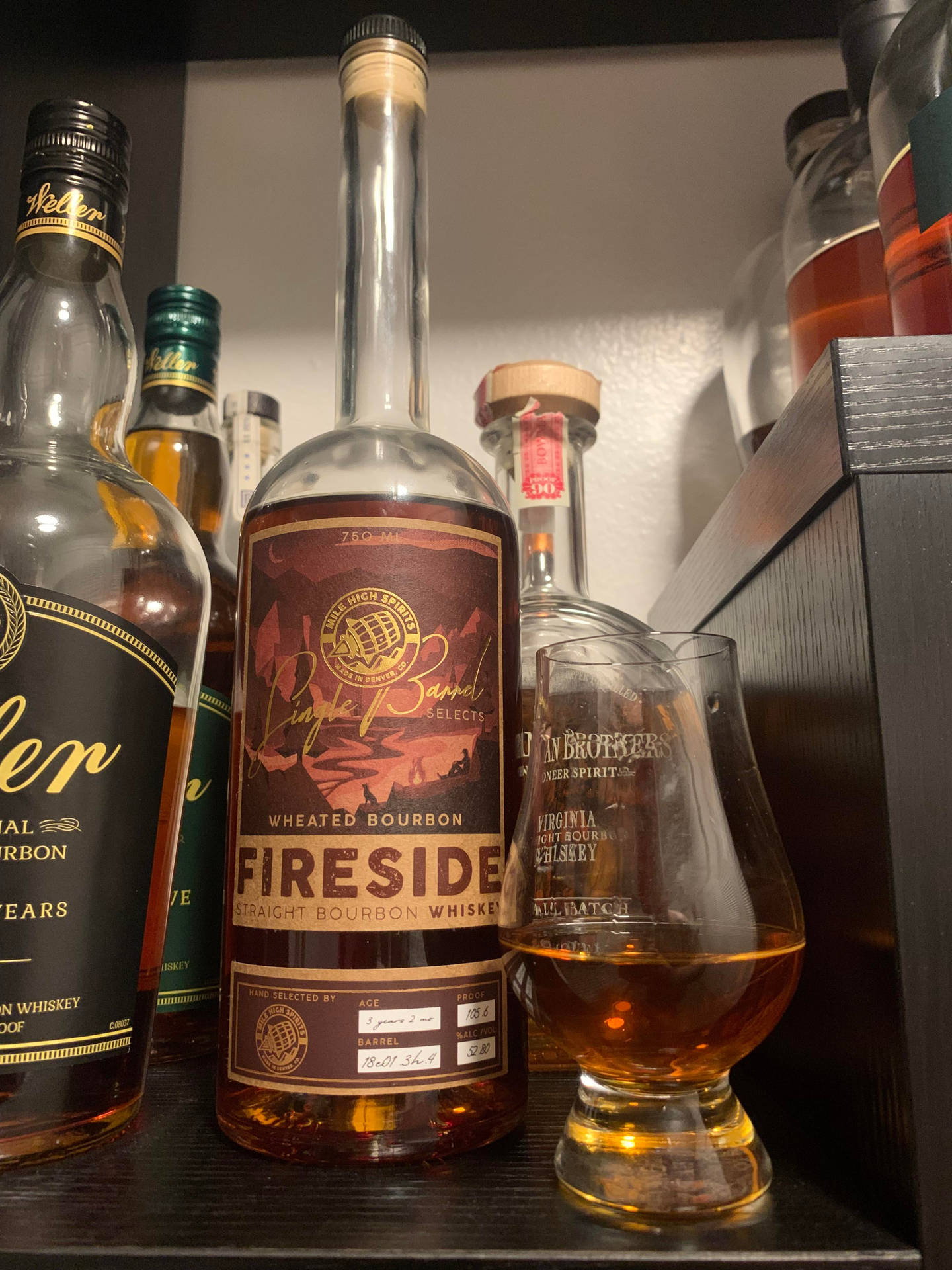 一瓶Fireside Wheated Bourbon Whiskey，旁邊放著品酒杯，置於酒架上。