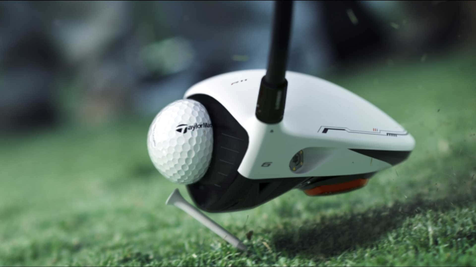 在高爾夫球場享受精彩時光 壁紙 — TaylorMade 高爾夫球桿在茂密的綠色發球台上擊打白色高爾夫球，草葉飛揚。