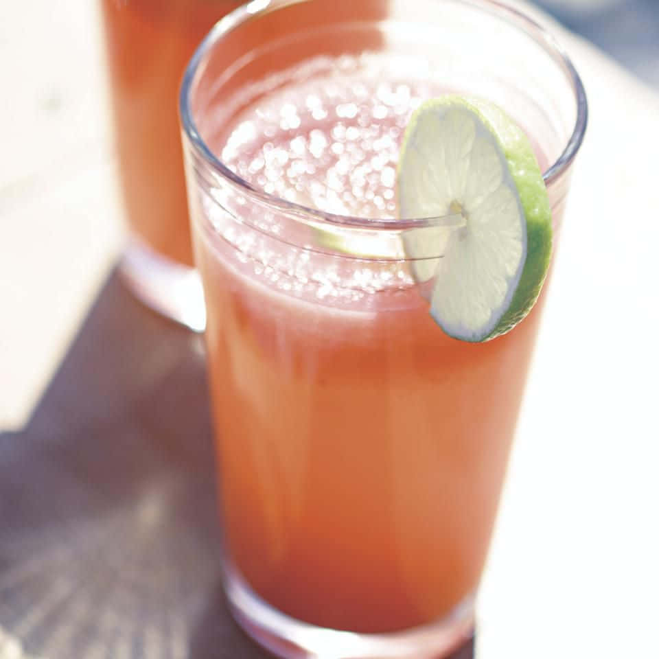 Beautiful Drink 桌布 壁紙 — 在高腳杯中，一款清爽的粉紅色飲品，配上青檸裝飾和冰塊氣泡，在明亮的陽光下。