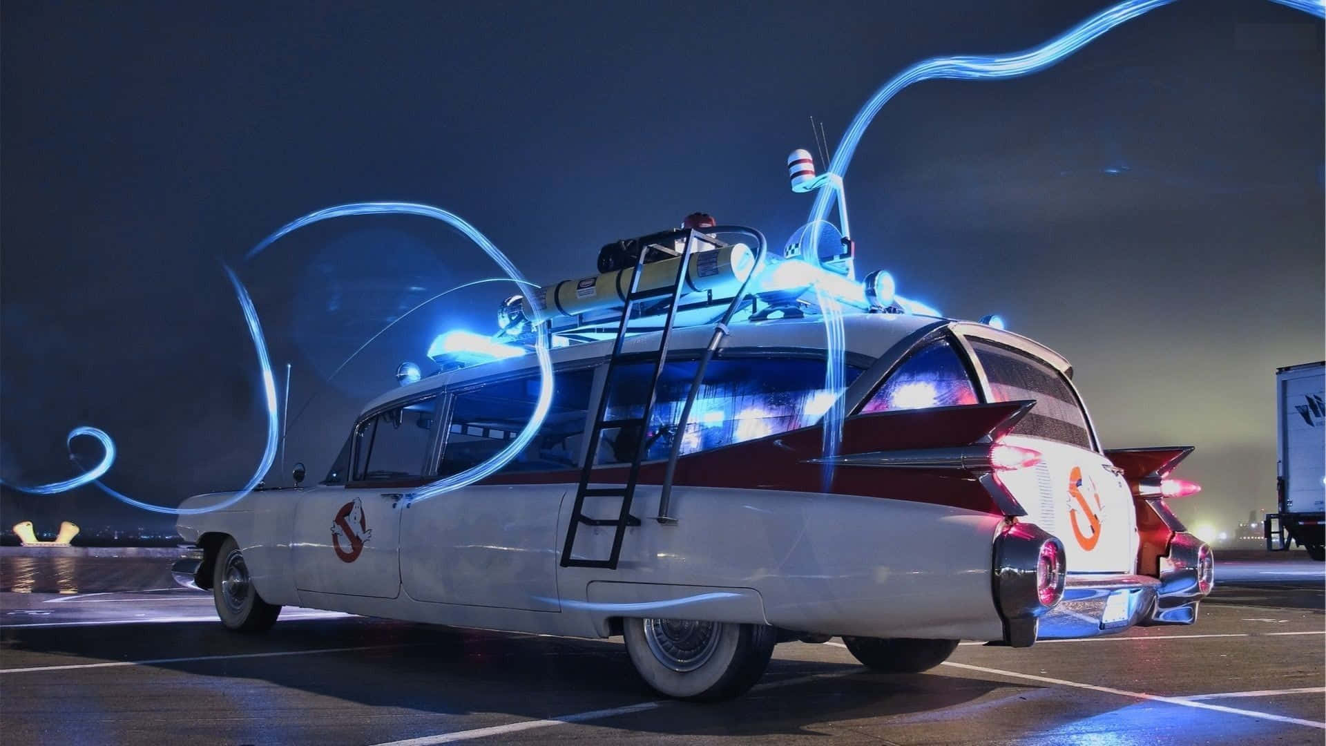 Ghostbusters 桌布 壁紙 — 在黑暗夜空下的停車場中，Ghostbusters Ecto 1 汽車散發出藍色能量軌跡。