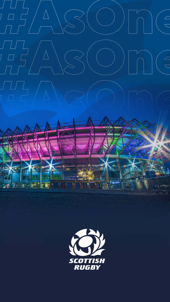 Scotland Rugby 桌布 壁紙 — 在黑暗天空下，一個現代欖球場被粉紅色、藍色和綠色燈光照亮的充滿活力的夜景。