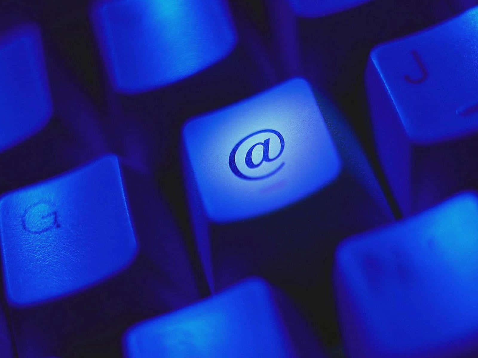 Email 桌布 壁紙 — 在黑暗環境中，發光藍色鍵盤的特寫，@ 符號顯著亮起。