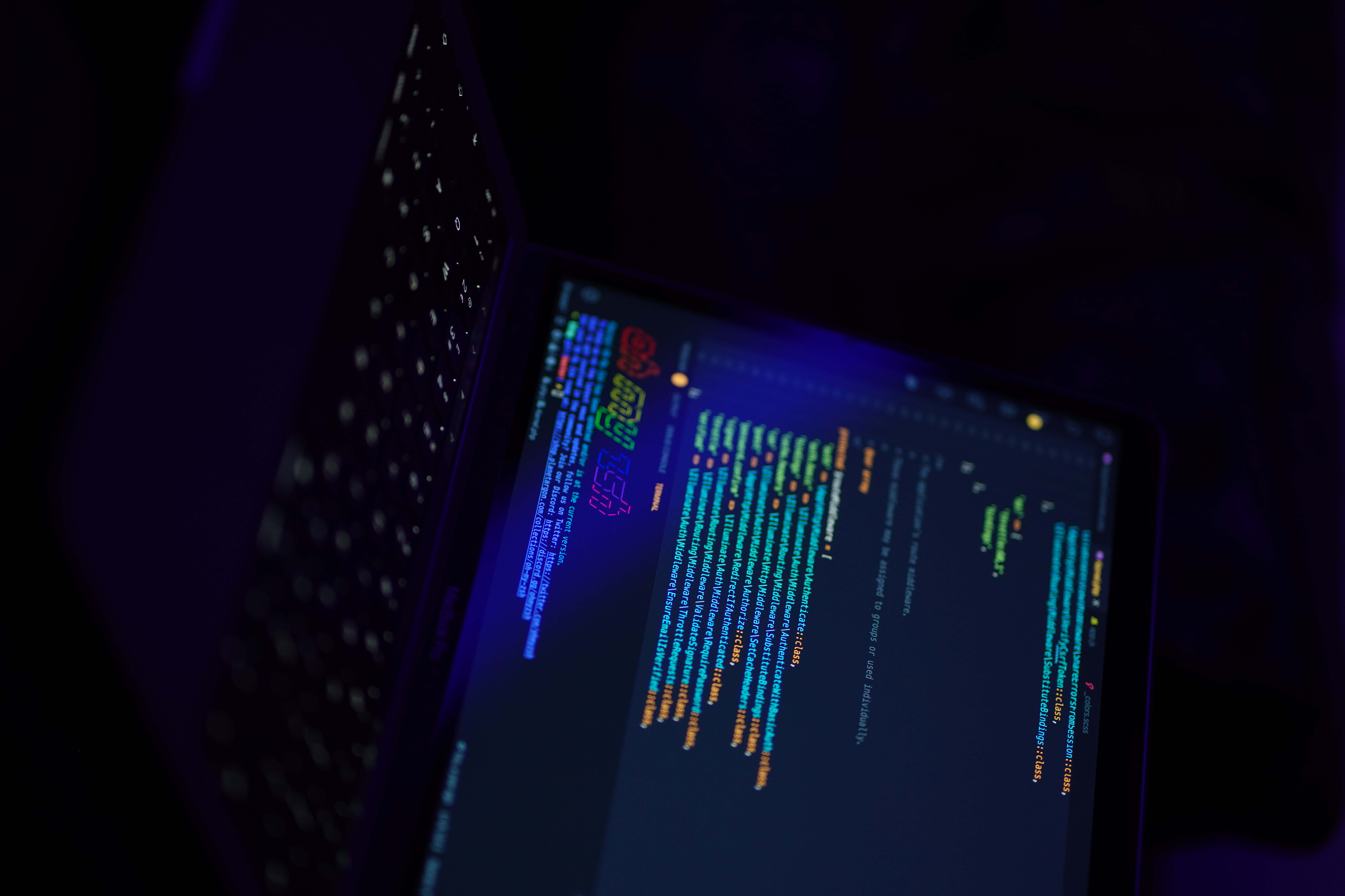 Visual Studio 桌布 壁紙 — 在黑暗的房間中，被藍光籠罩的筆記型電腦螢幕閃爍著彩色代碼。