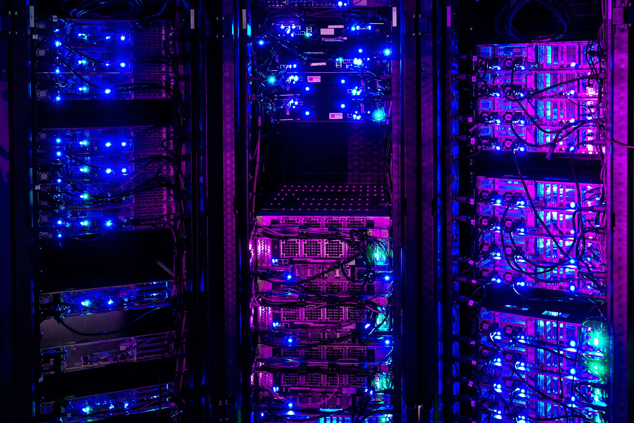 Gaming Servers 桌布 壁紙 — 在黑暗的數據中心，一排排伺服器機架閃爍著鮮豔的藍色和紫色LED燈光。