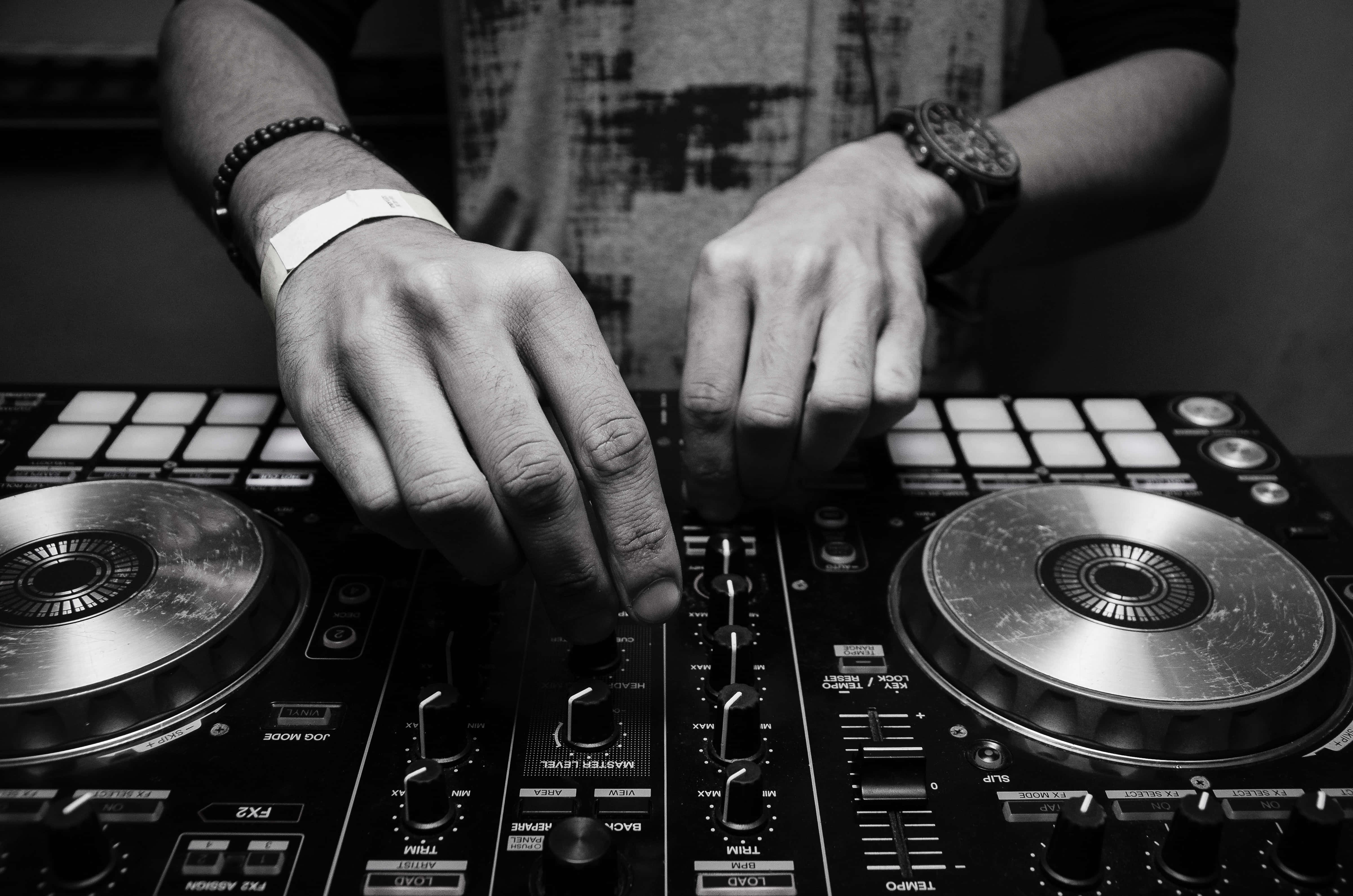 DJ 桌布 壁紙 — 在黑白照片中，DJ 的雙手熟練地操作專業混音器上的旋鈕和唱盤。