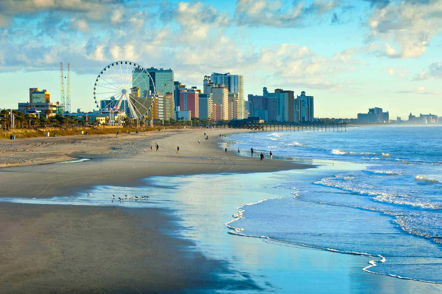 日落時的海灘，海浪，摩天輪和城市天際線。