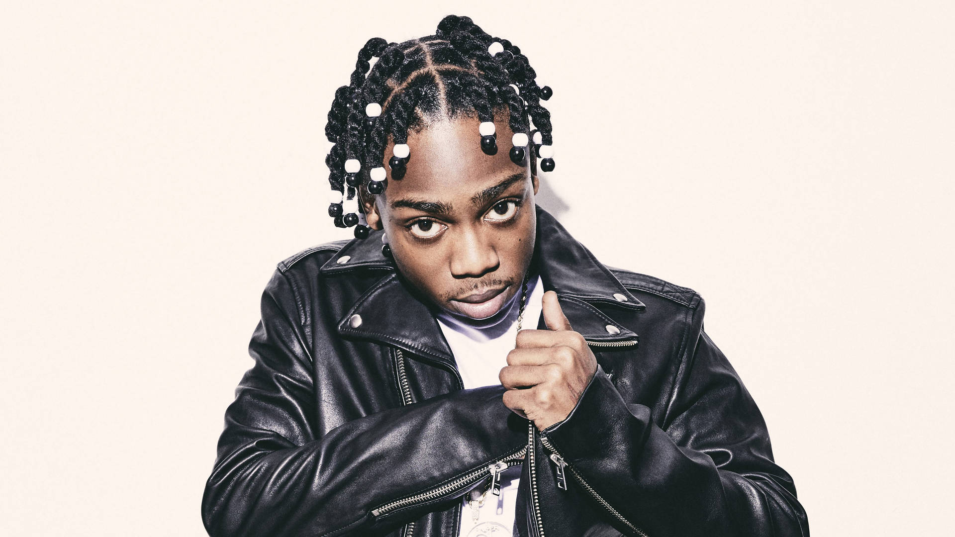 年輕男子身穿黑色皮夾克，辮子頭髮和白色珠子，豎起大拇指。