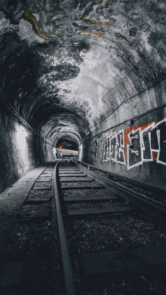 地下火車隧道塗鴉 壁紙 — 一條粗糙的鐵路隧道，牆壁佈滿塗鴉，路軌通向盡頭的遠處光線。
