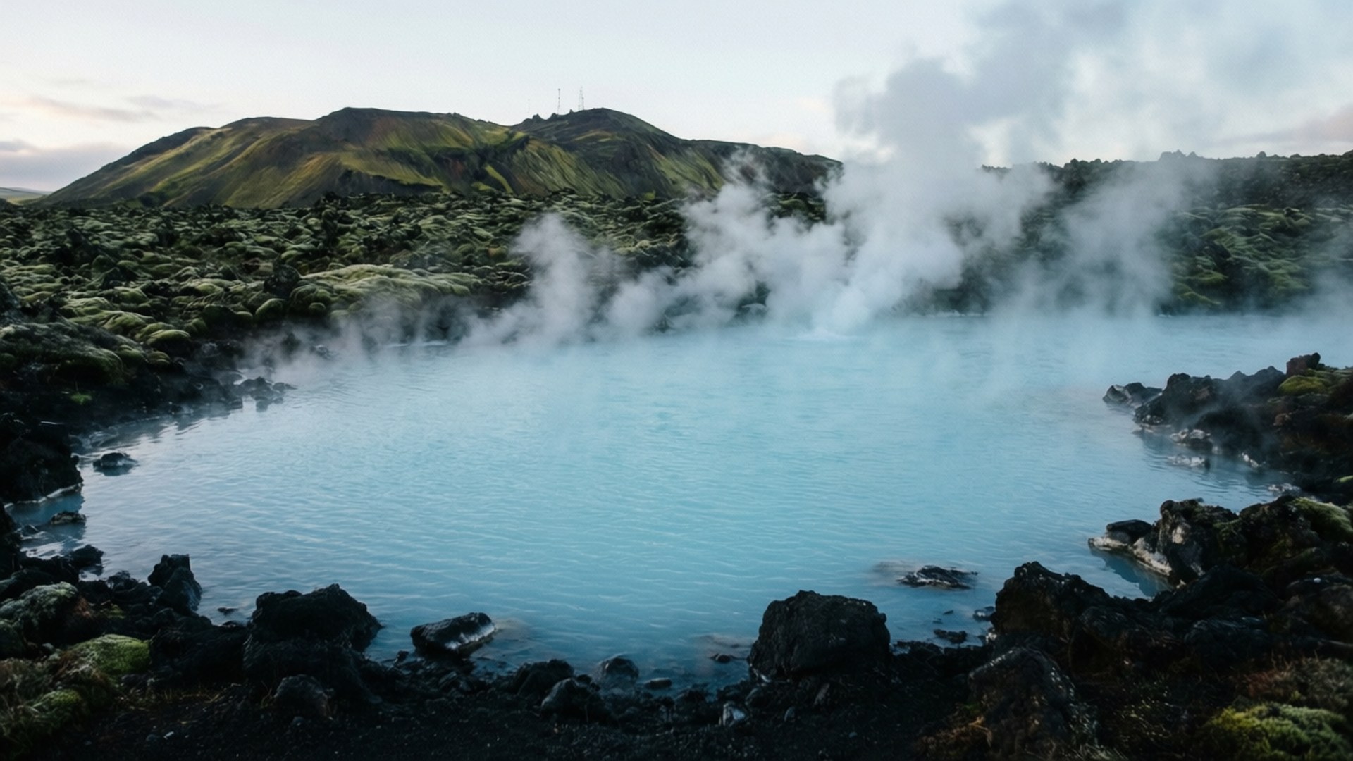 藍綠色地熱池，蒸氣從火山岩和背景中的綠色山丘升起。