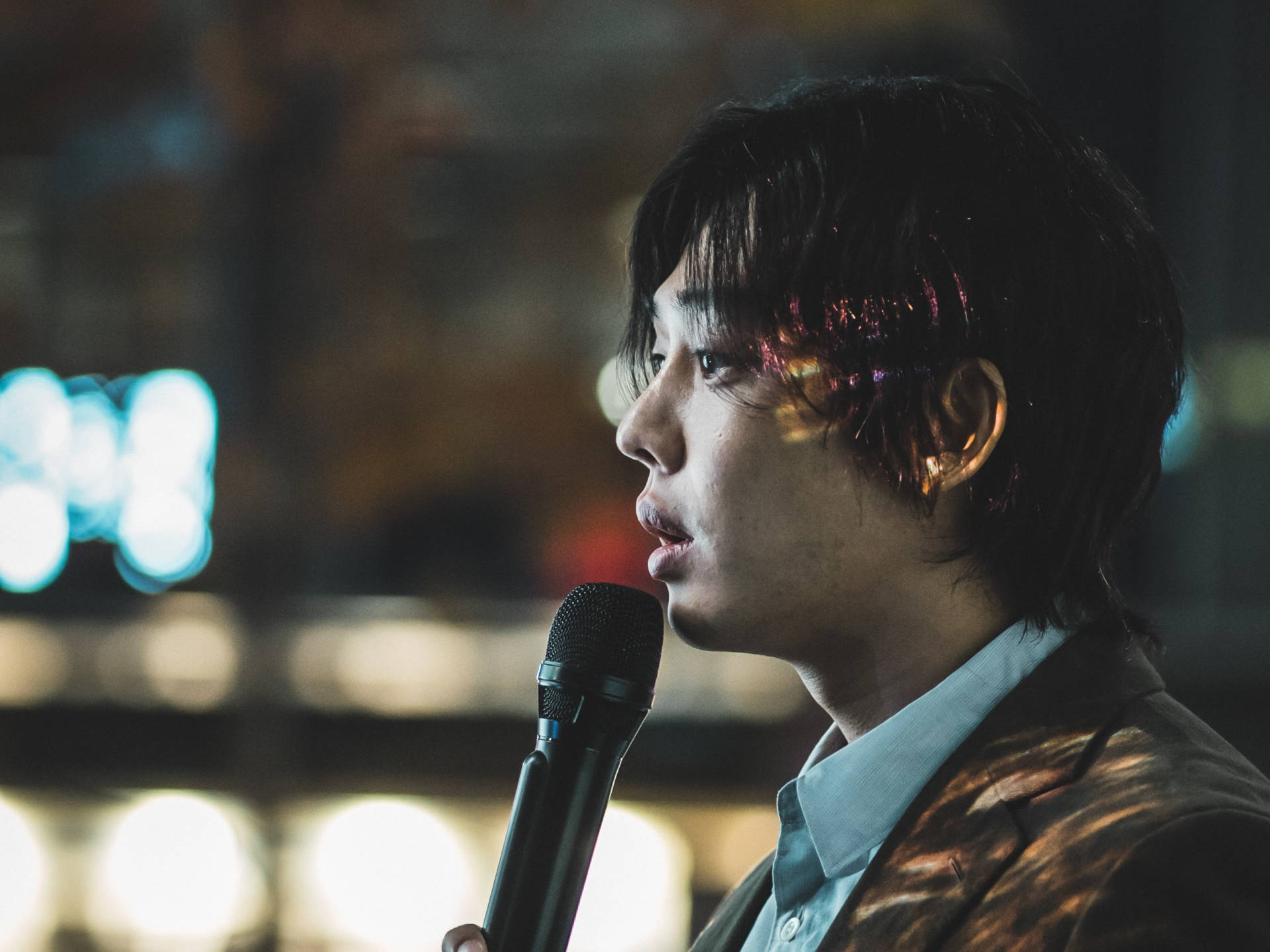 年輕男子在夜晚對著麥克風唱歌，背景是城市燈光