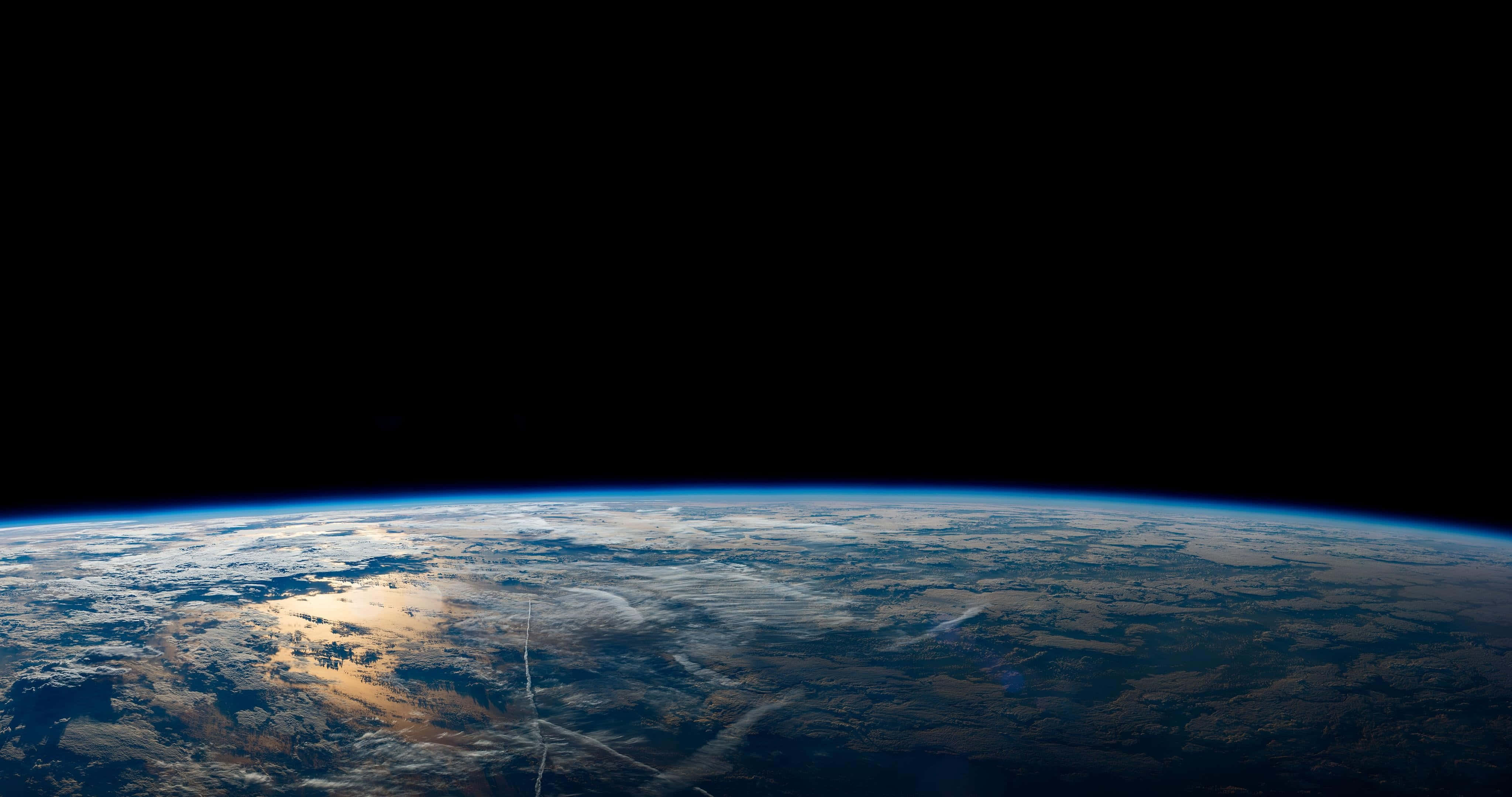 地球上方厚重白雲背景 壁紙 — 地球在太空的黑色虛空中輕輕彎曲，帶有旋轉的雲層和發光的大氣邊緣。