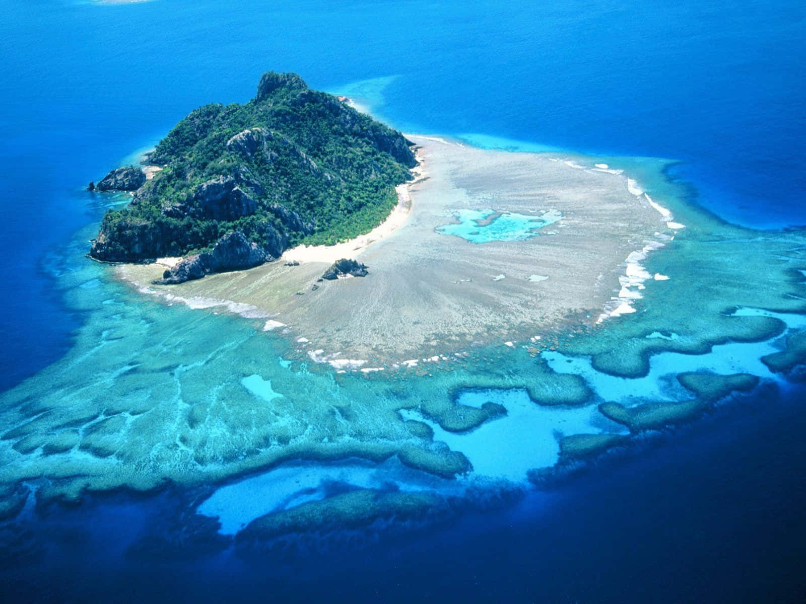 地球上的天堂：絕美島嶼風景 壁紙 — 俯瞰一個鬱鬱蔥蔥的綠色島嶼，周圍環繞著充滿活力的綠松石珊瑚礁和深藍色海洋。