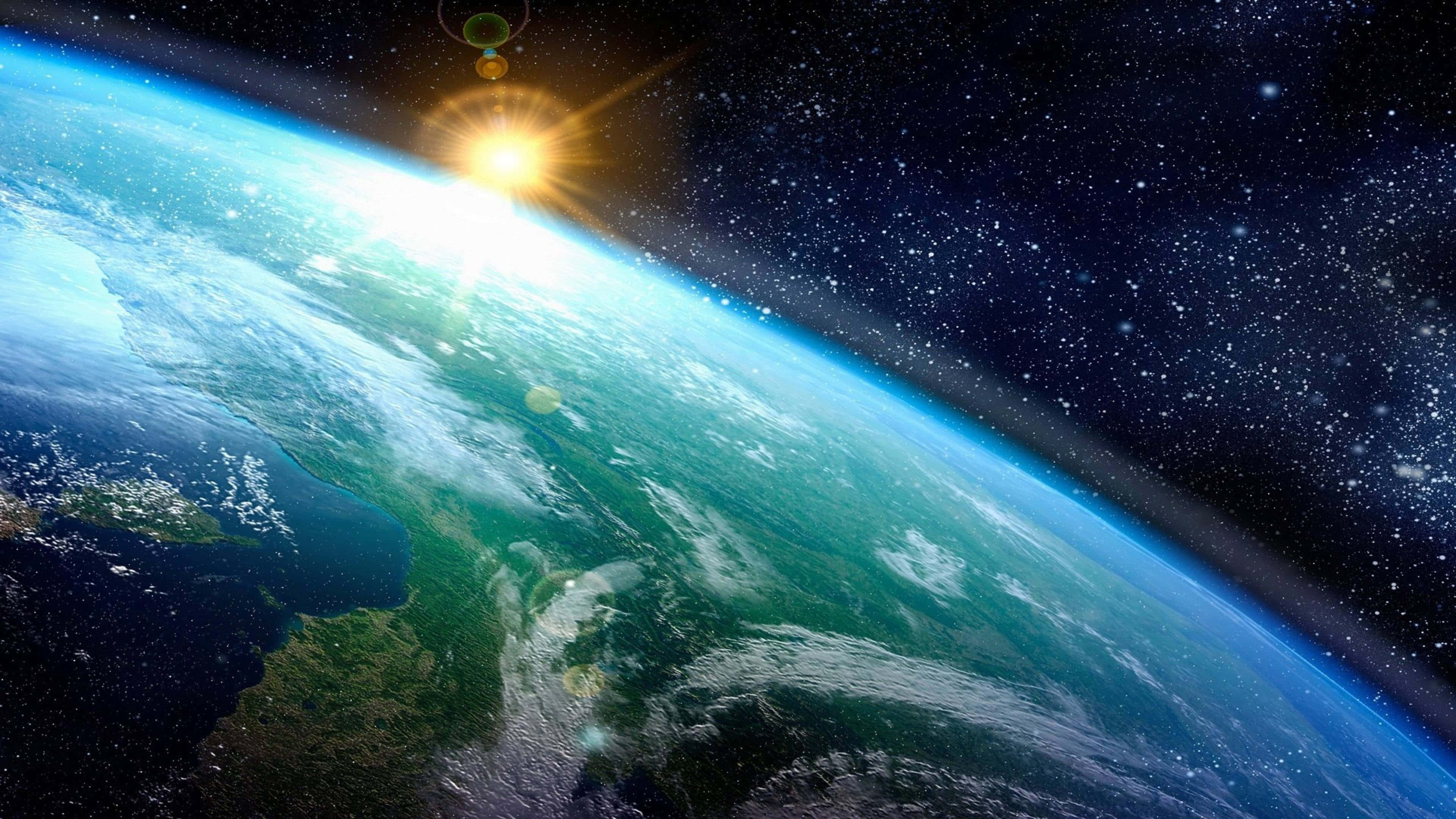 4K Ultra HD 桌布 壁紙 — 地球在太空中雄偉地彎曲，陽光爆發照亮海洋、大陸和虛空中閃爍的星星。