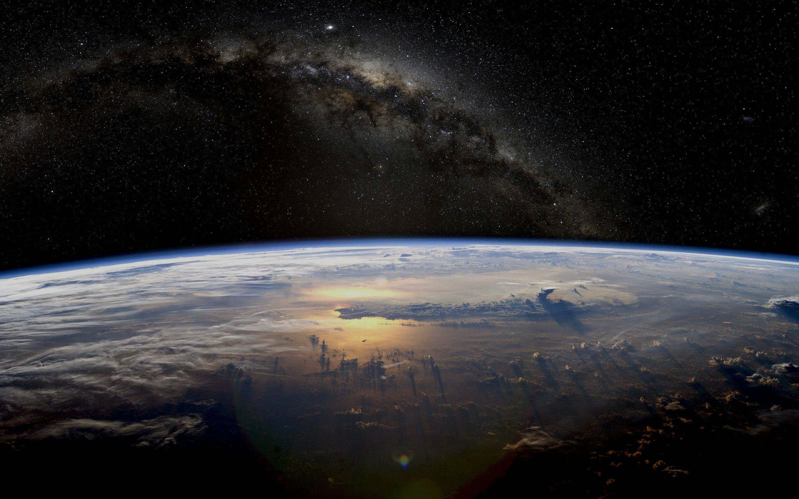 Atmosphere 桌布 壁紙 — 地球在星空下彎曲，銀河在頭頂拱起，陽光在雲層上閃爍。