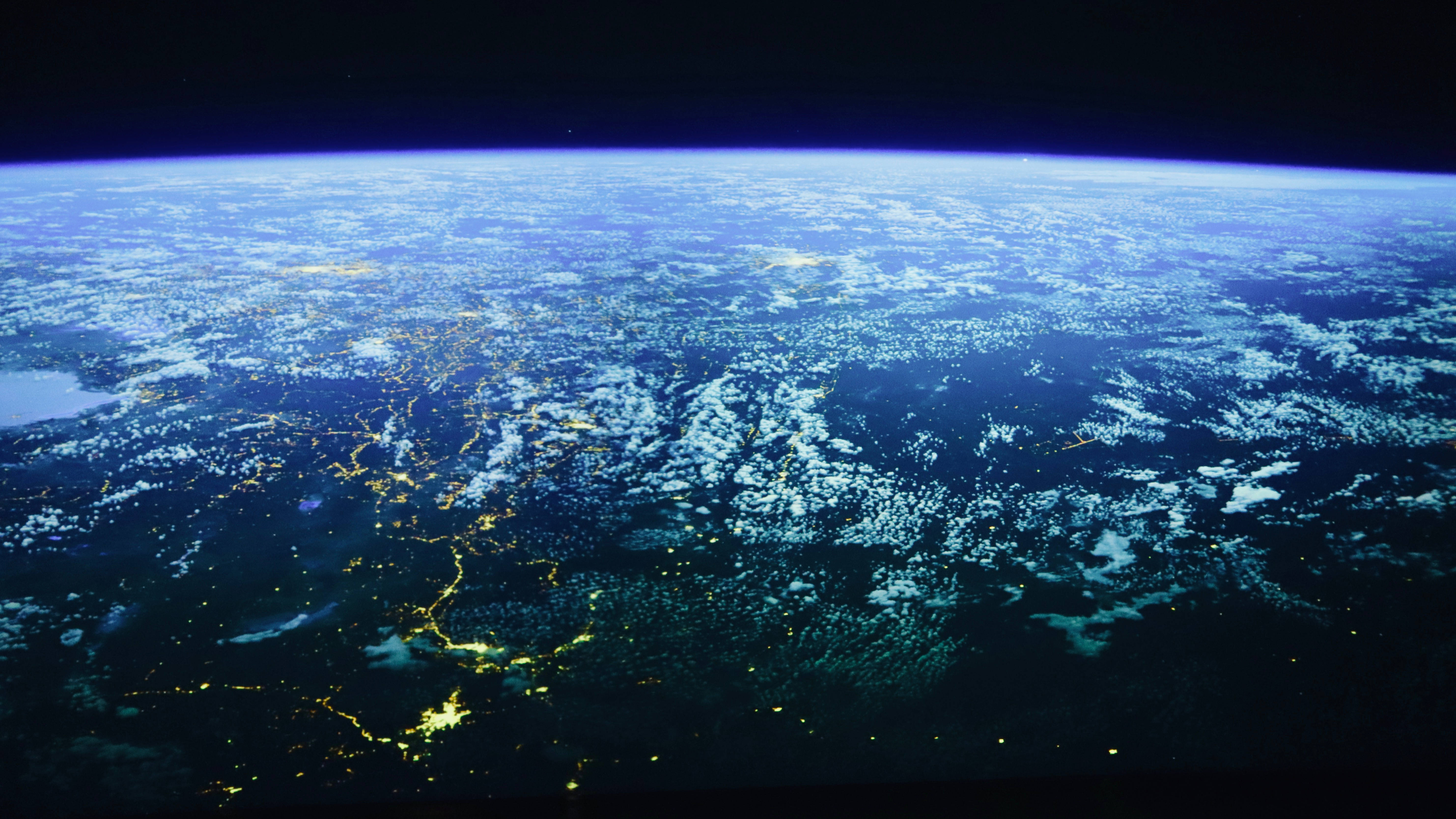 地球太空視角 文明：地球之外 壁紙 — 從太空觀看夜晚的地球，城市燈光閃爍，雲層旋轉，背景是黑暗的宇宙。