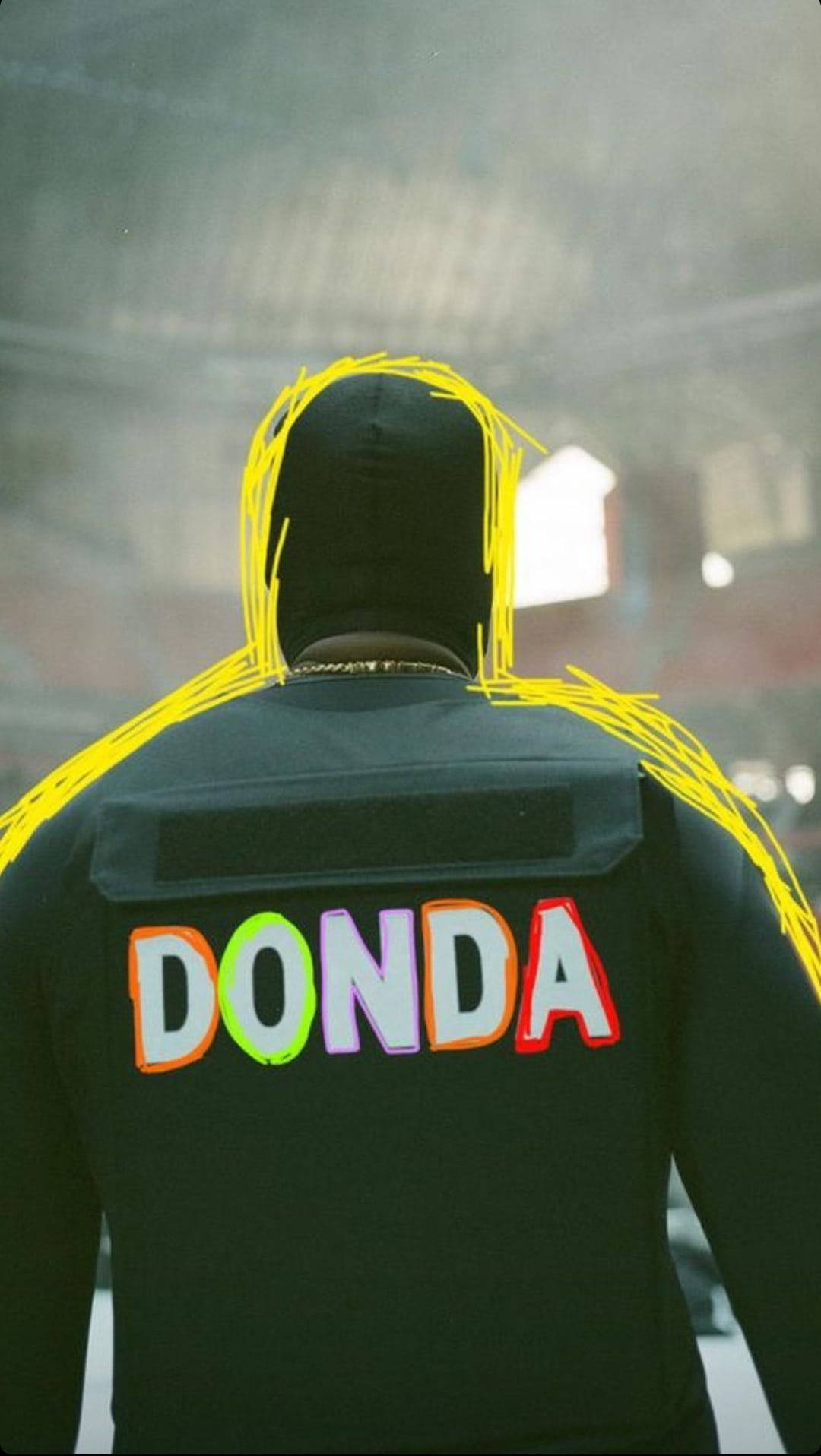 一個人穿著黑色連帽衫，上面有彩色字母和黃色塗鴉寫著「DONDA」。