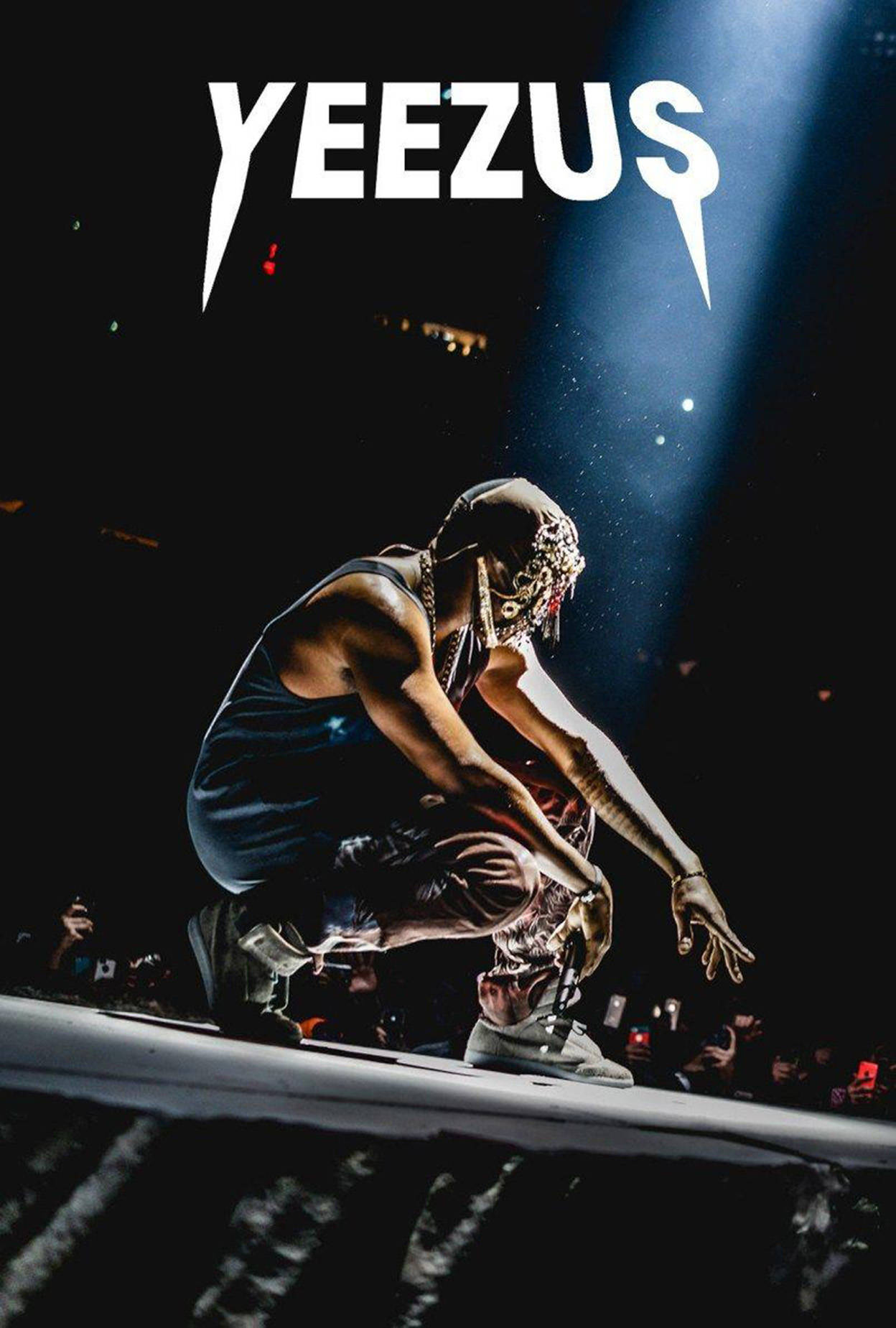 坎耶·威斯特《Yeezus》專輯封面 iPhone 壁紙 — 一位說唱歌手在黑暗的演唱會場景中，蹲在舞台上，聚光燈下，上方有 'YEEZUS' 文字。