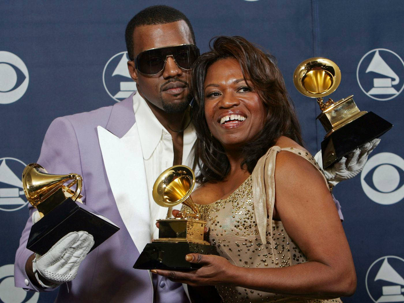 坎耶·威斯特在《Donda》的生與死中 壁紙 — Kanye West 和他的母親 Donda West 在帶有標誌的藍色背景前自豪地微笑著手持格林美獎項。