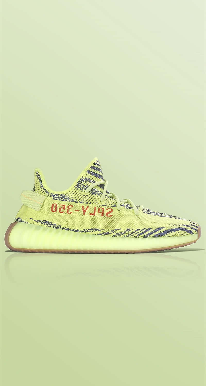 淡綠色背景上，帶有深藍色圖案和紅色文字的青檸綠色Yeezy 350運動鞋。