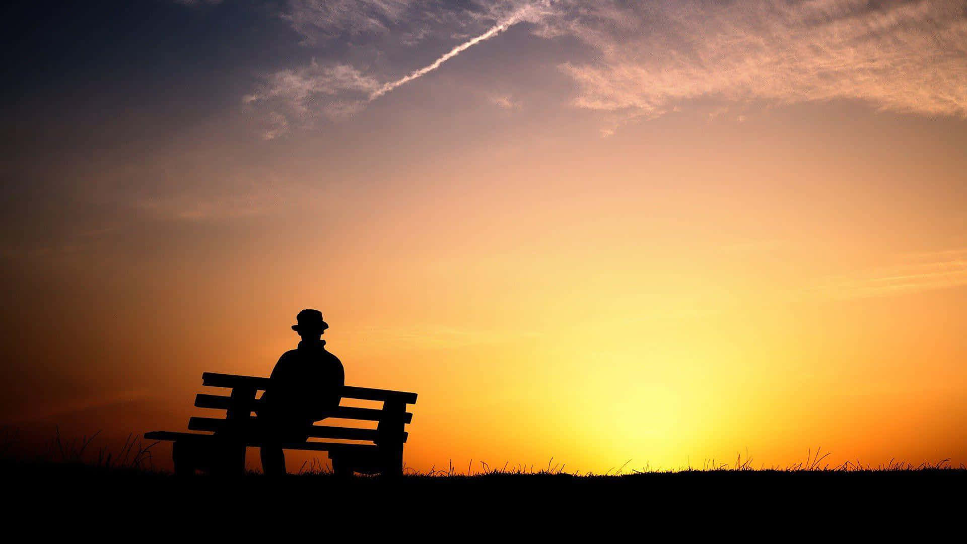 戴帽人物坐在長椅上觀看夕陽落在草地上。