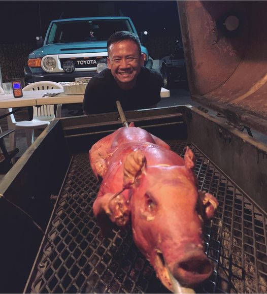 男子夜間在戶外烤全豬，背景有車