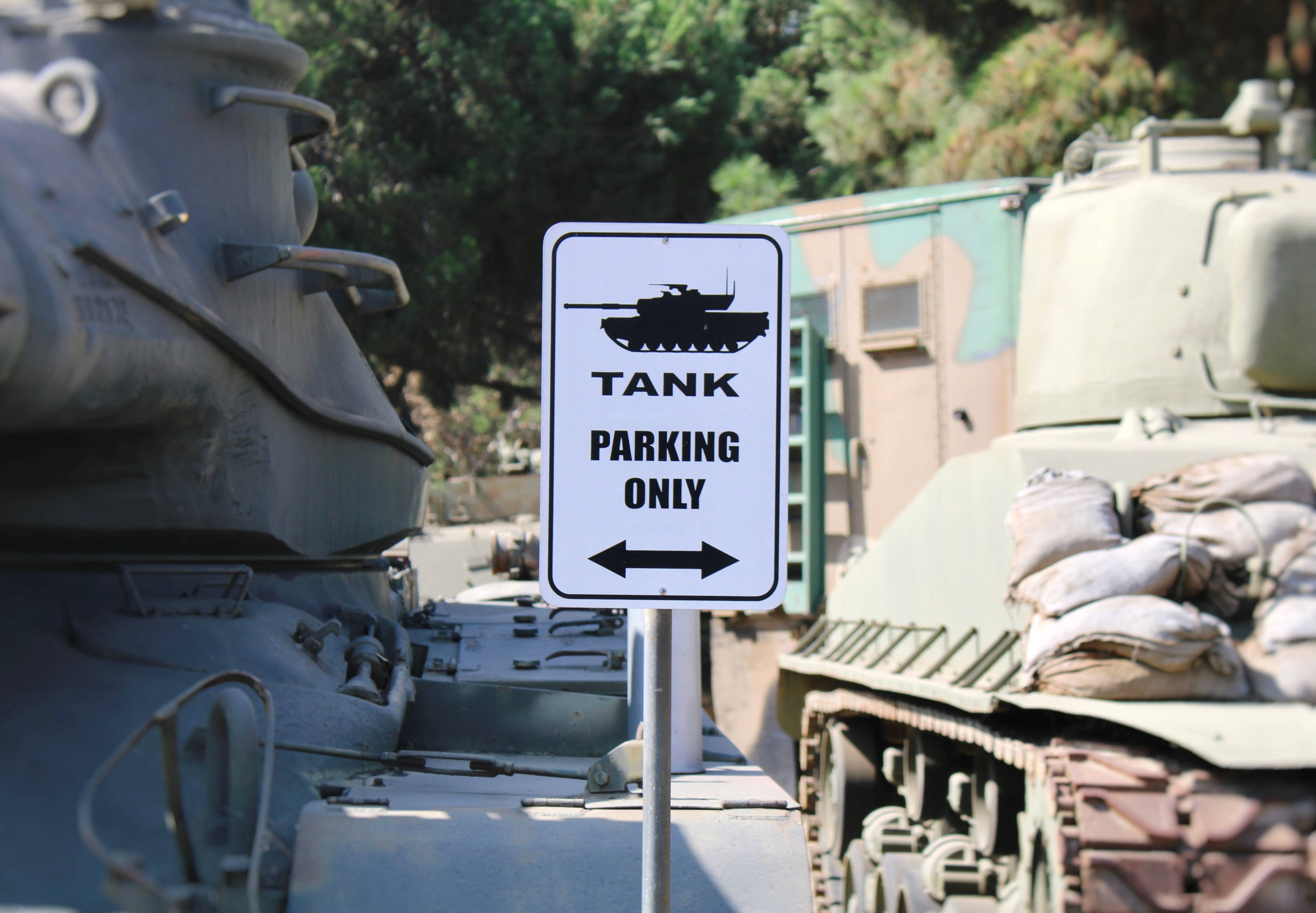 坦克停車場 壁紙 — 一個白色標誌寫著「TANK PARKING ONLY」，在明亮的日光下矗立在兩輛軍用坦克之間。