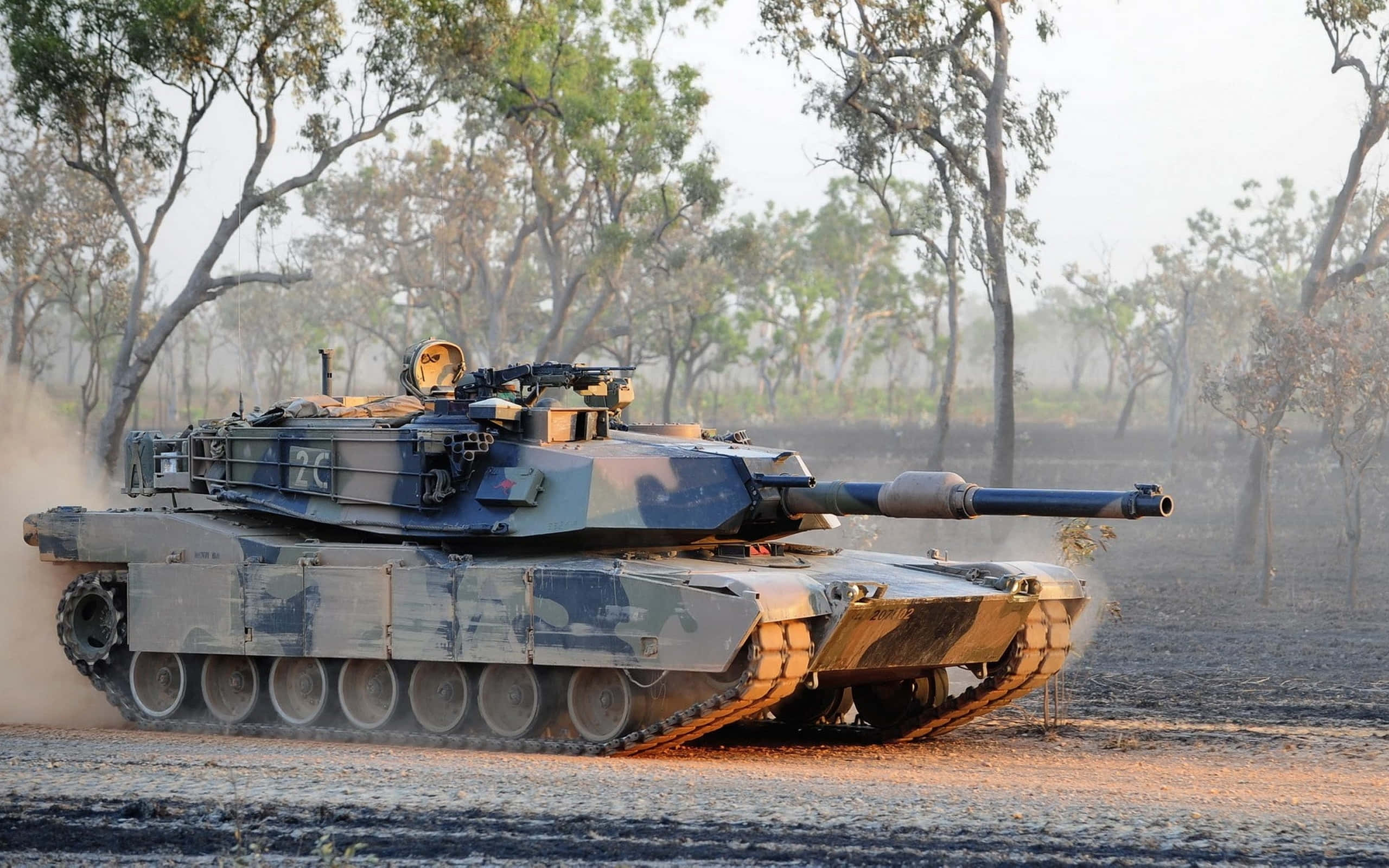 坦克的力量 壁紙 — 一輛迷彩軍用坦克在塵土飛揚的田野中行駛，背景有稀疏的樹木。