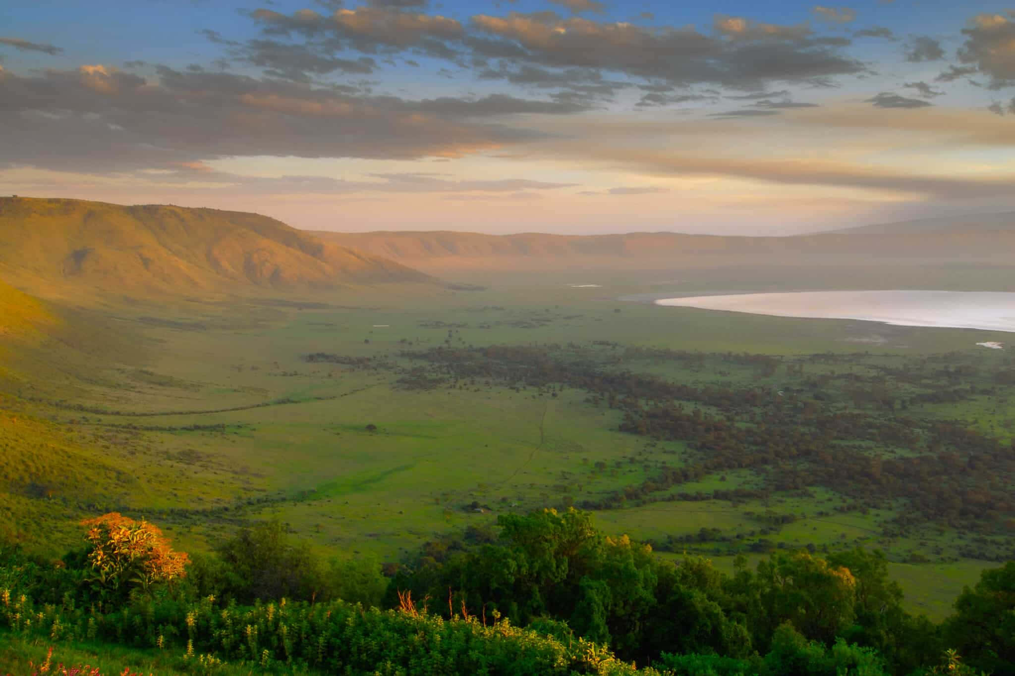 坦桑尼亞北部恩戈羅恩戈羅火山口的美麗風景 壁紙 — 夕陽灑落在廣闊的綠色山谷，起伏的丘陵和寧靜的湖泊在柔和的雲朵下。